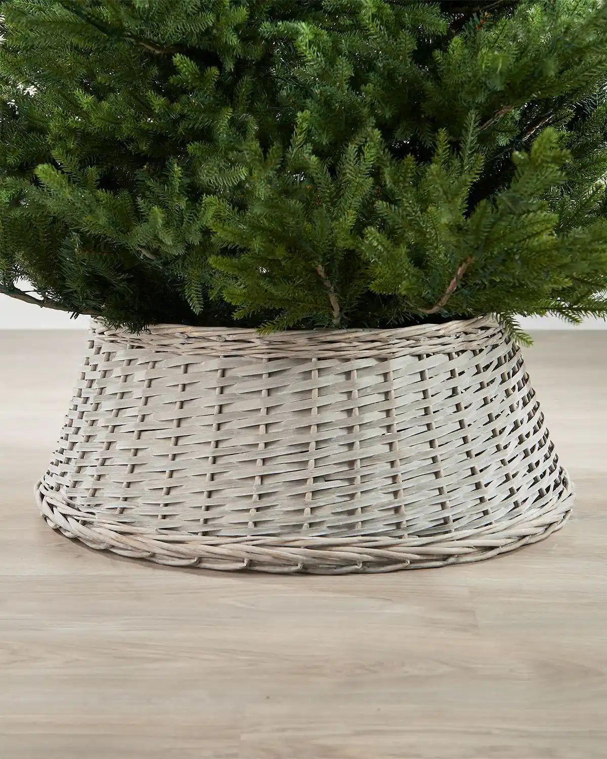 70cm grey wicker tree collar placed around the base of a Christmas tree on an indoor wooden floor.