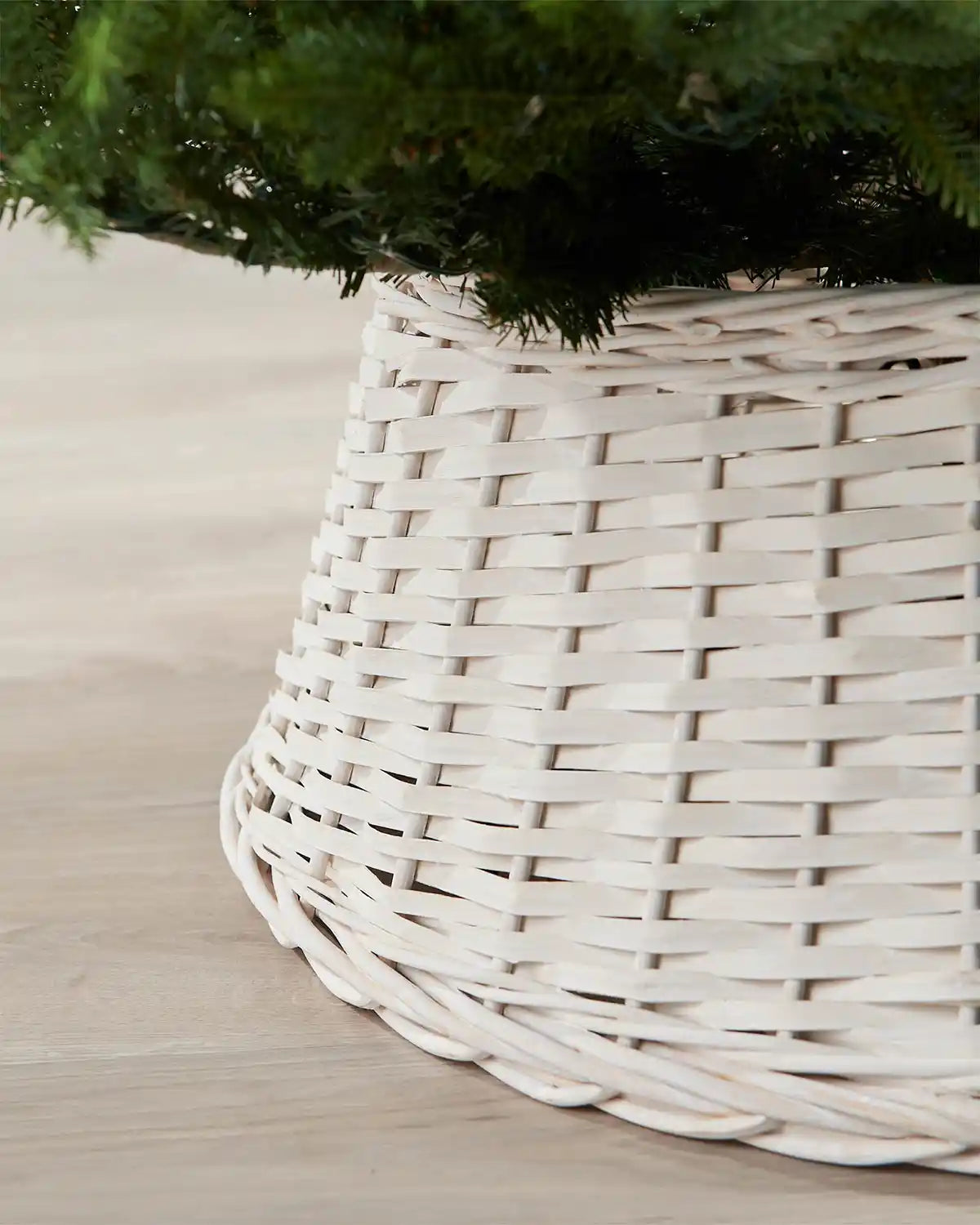 Close-up of the 70cm off-white wicker tree collar showing the woven rattan texture beneath green Christmas tree branches.