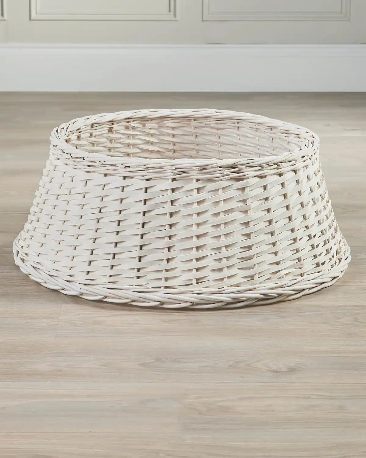 70cm off-white wicker tree collar displayed indoors on a wooden floor, showing its tapered shape and open top.