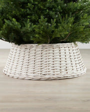 70cm off-white wicker tree collar placed around the base of a Christmas tree on an indoor wooden floor.