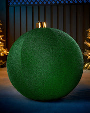 Large green 76cm inflatable tinsel Christmas bauble with a gold cap in an outdoor festive display.