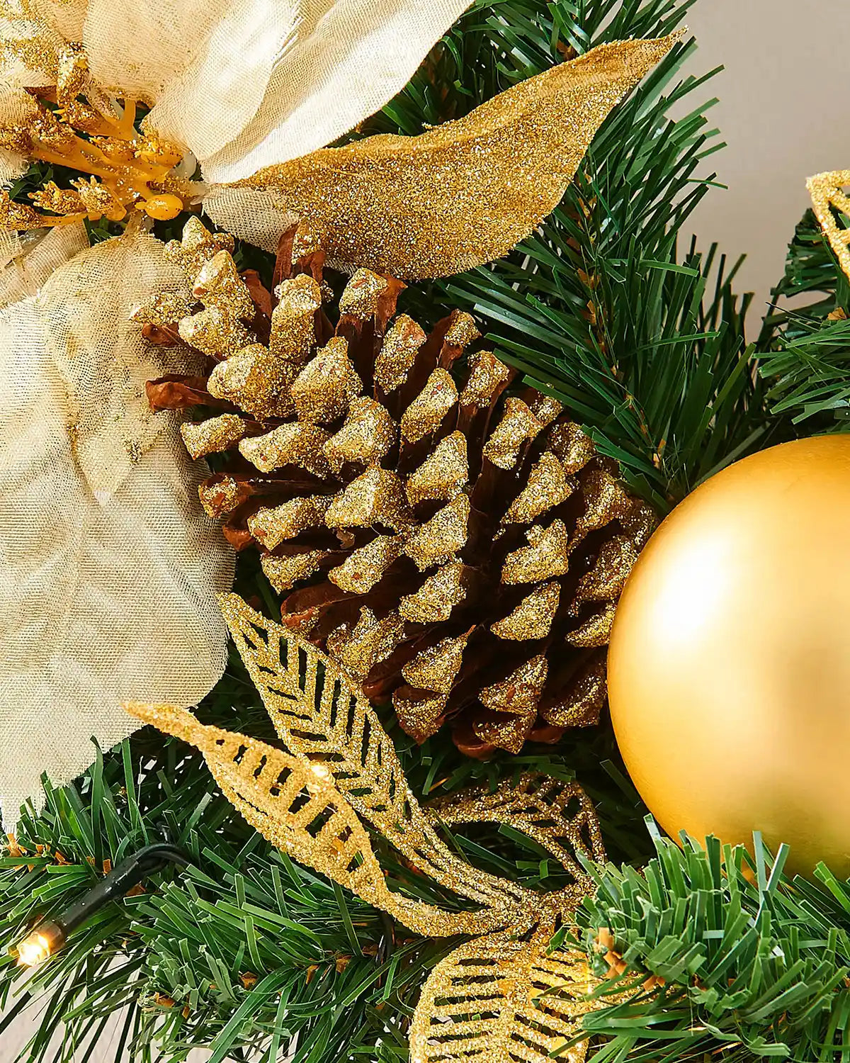 Close-up of a gold-tipped pinecone, gold bauble and glitter leaves on the pre-lit Christmas wreath