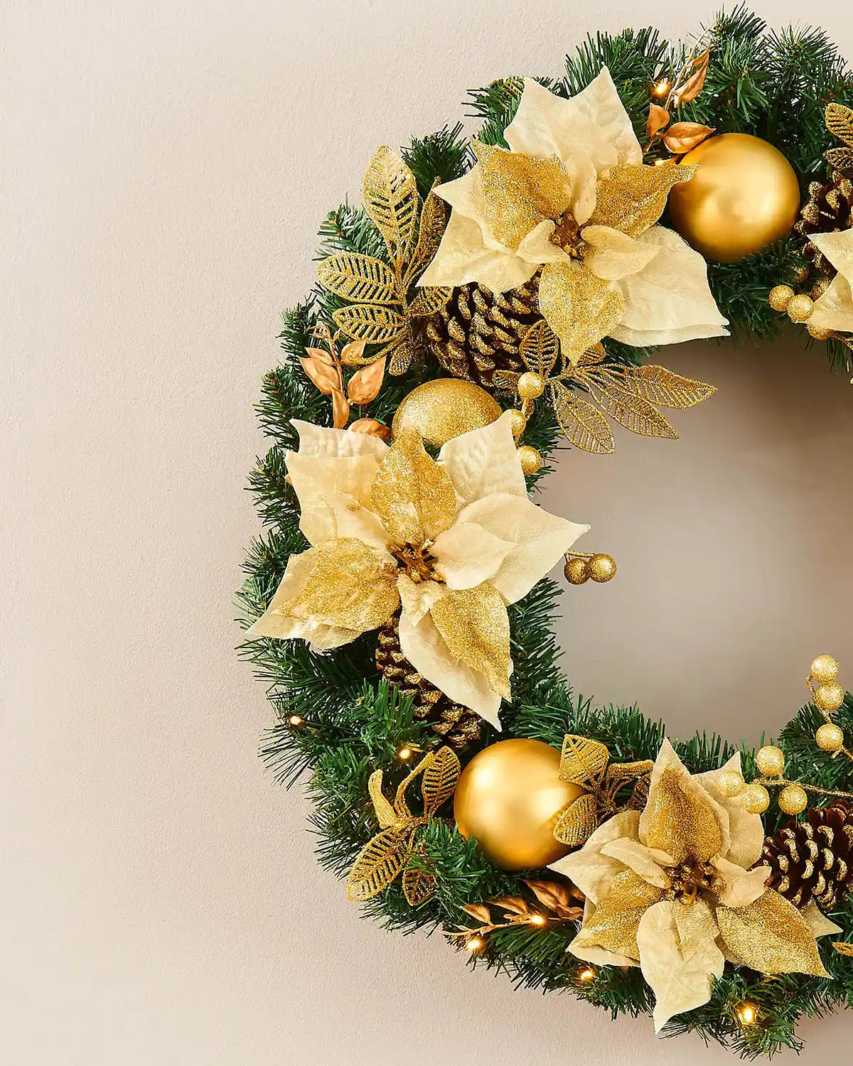Detail of cream and gold poinsettias, gold baubles and warm white lights on the Christmas wreath