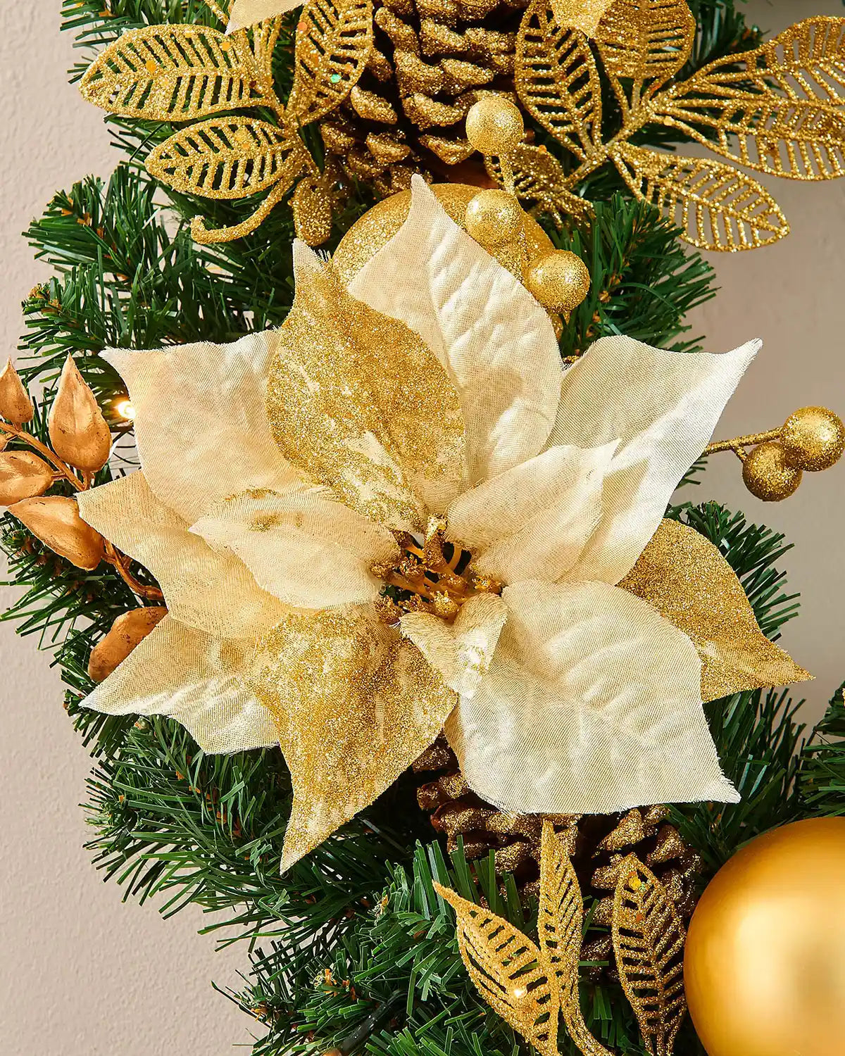 Close-up of a cream and gold poinsettia with glitter leaves and berries on the Christmas wreath