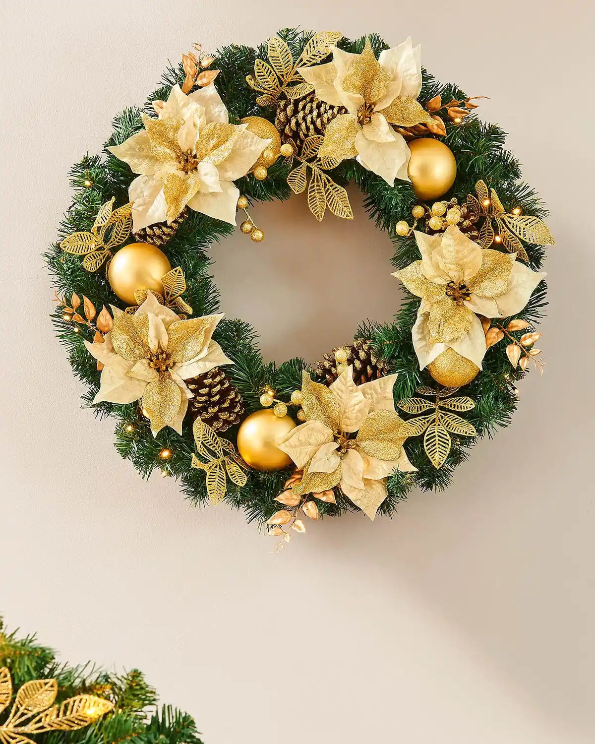 Extra thick cream and gold pre-lit Christmas wreath styled on a wall with warm white lights
