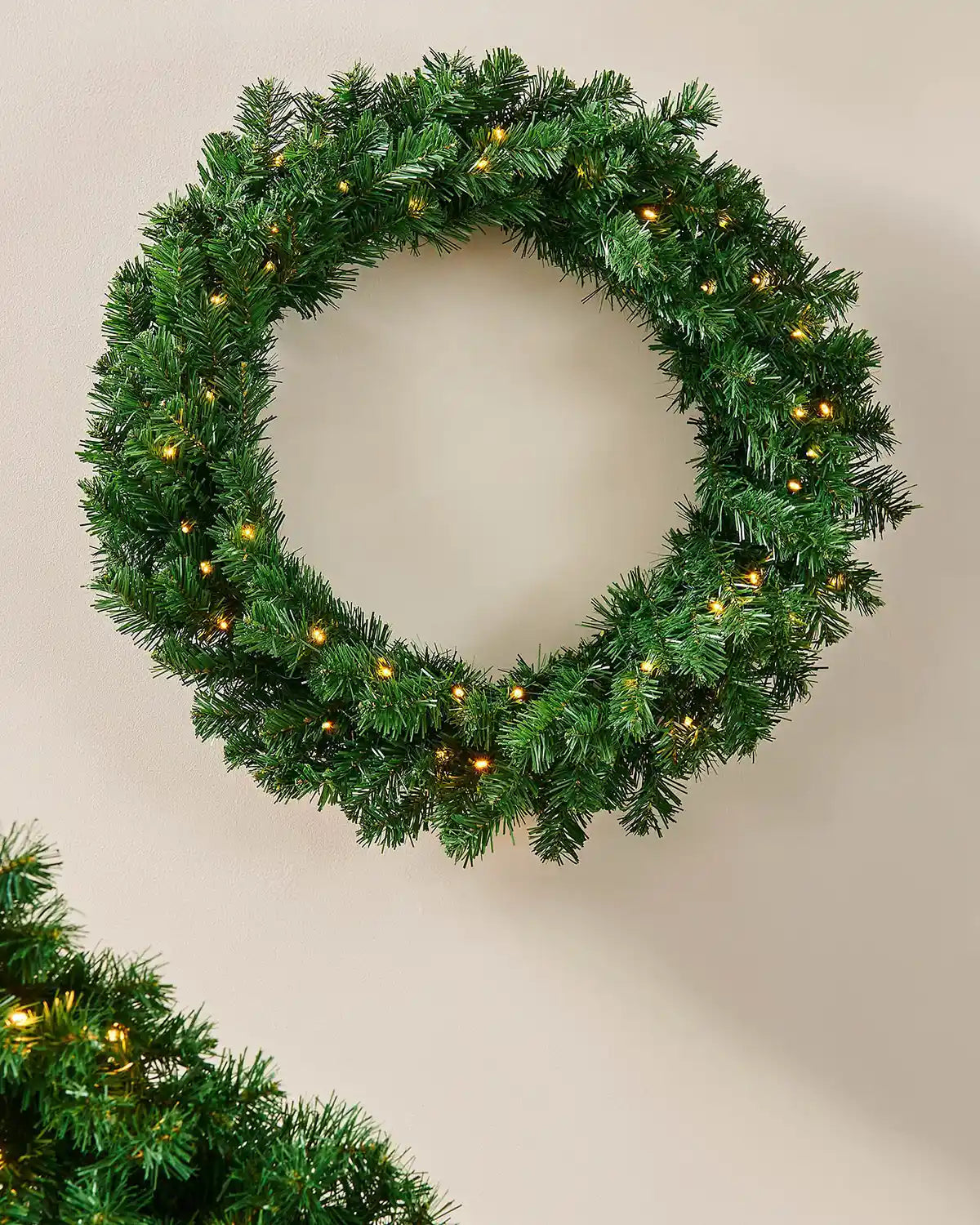 Extra thick green pre-lit Christmas wreath styled on a wall with warm white lights