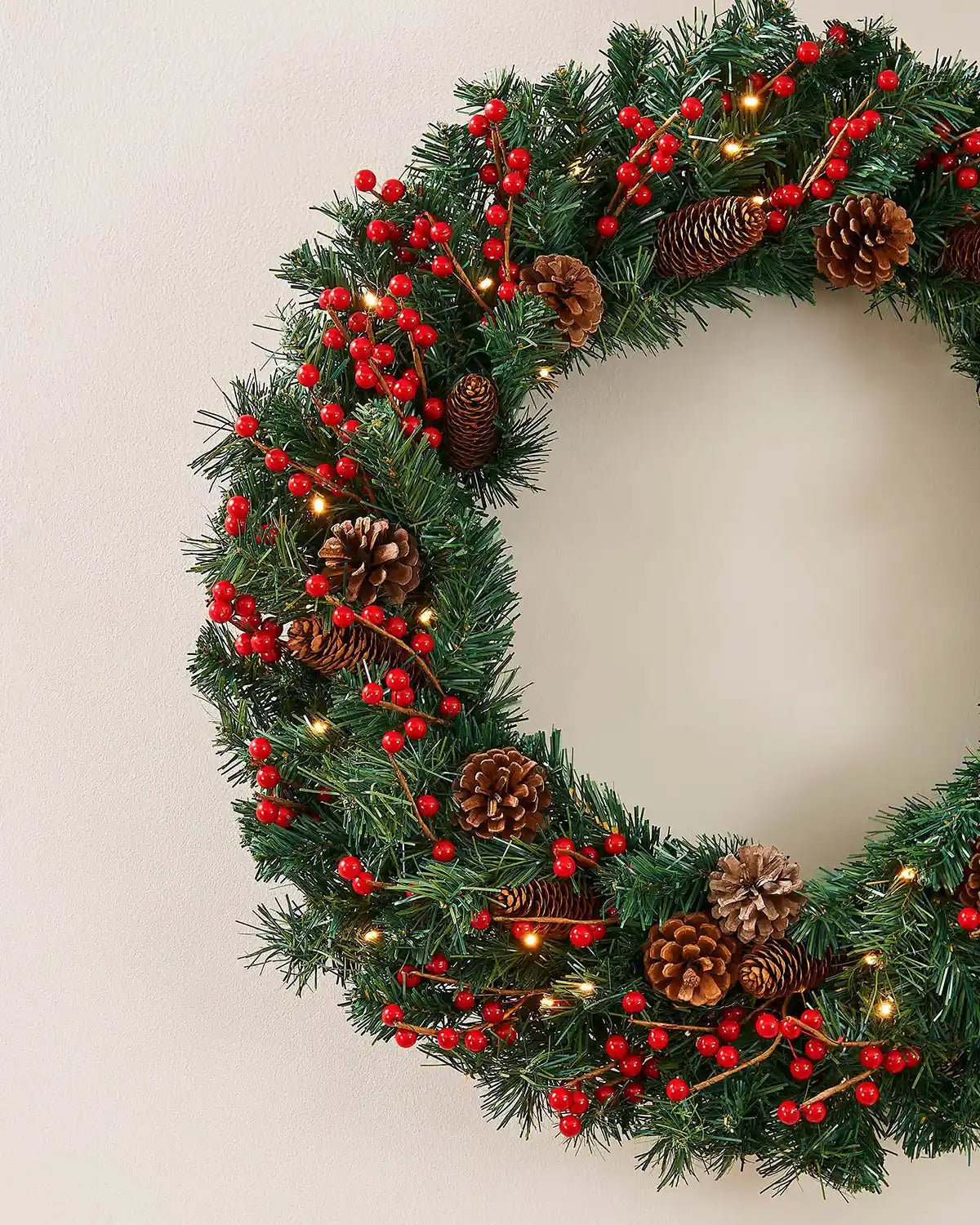 Detail of red berries, pinecones and warm white lights on the extra thick Christmas wreath