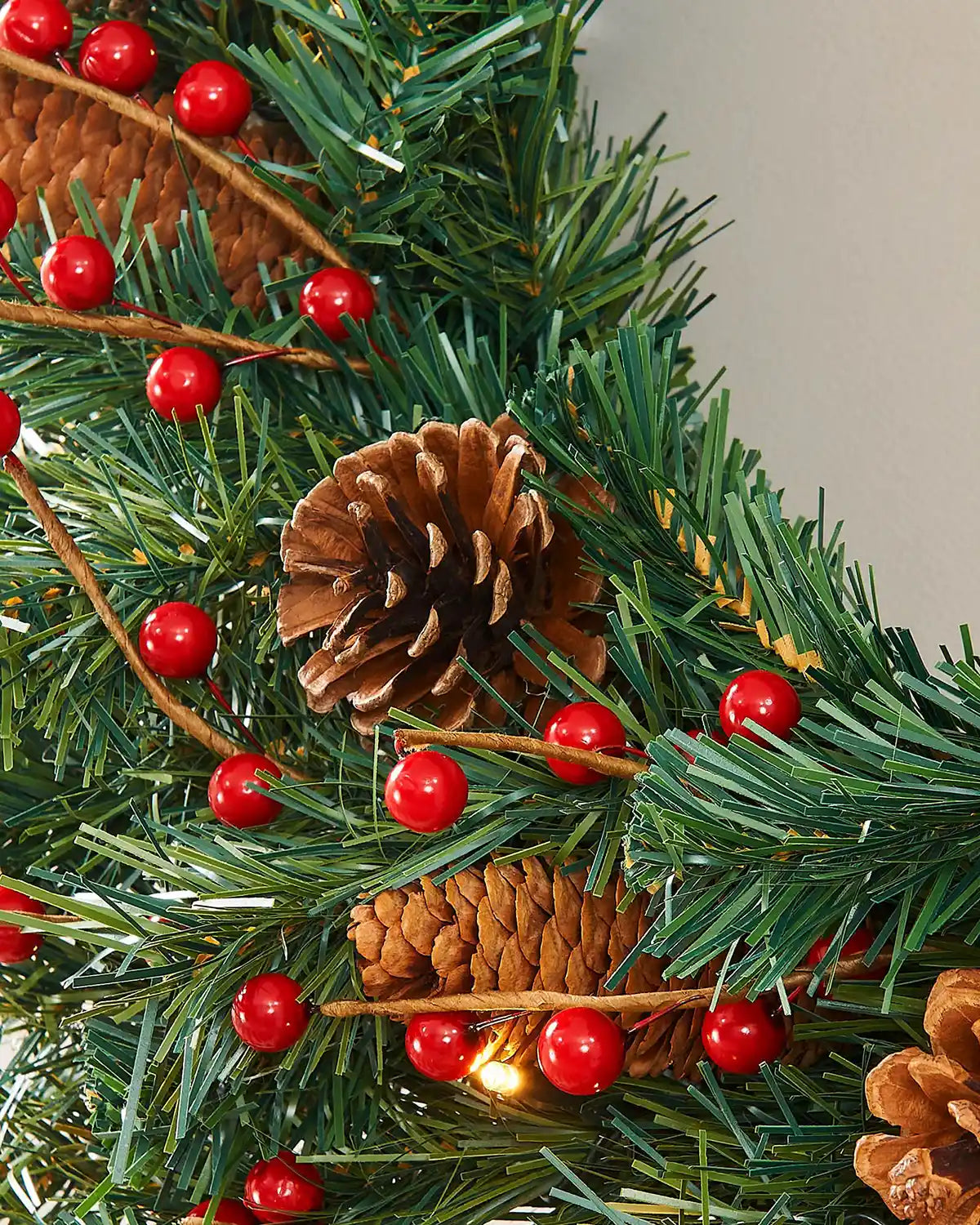 Close-up of pinecones and red berries arranged among the green wreath foliage