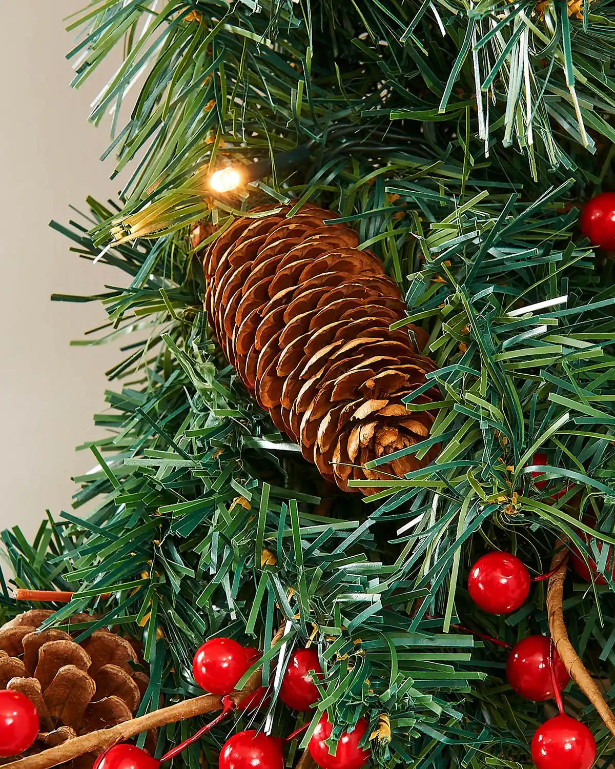 Close-up of a pinecone, red berries and warm white LED light on the Christmas wreath