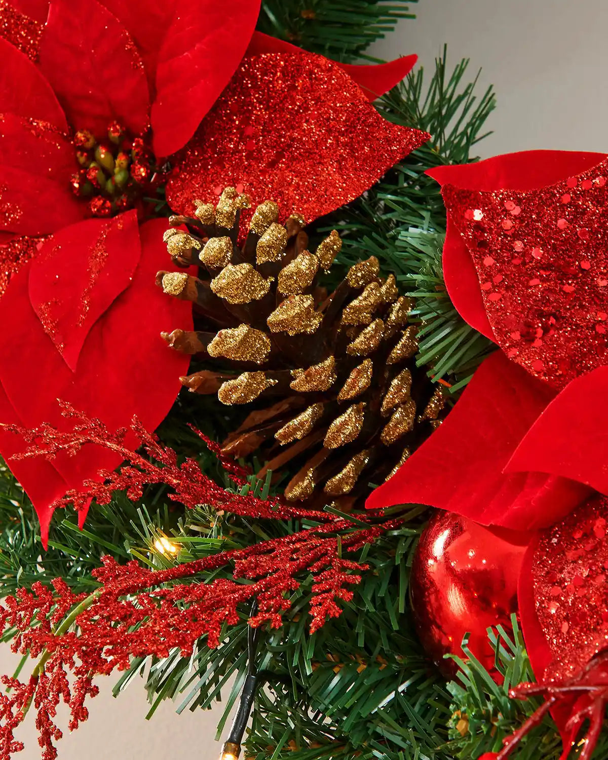 Detail of a gold-tipped pinecone, red poinsettias and warm white lights on the Christmas wreath