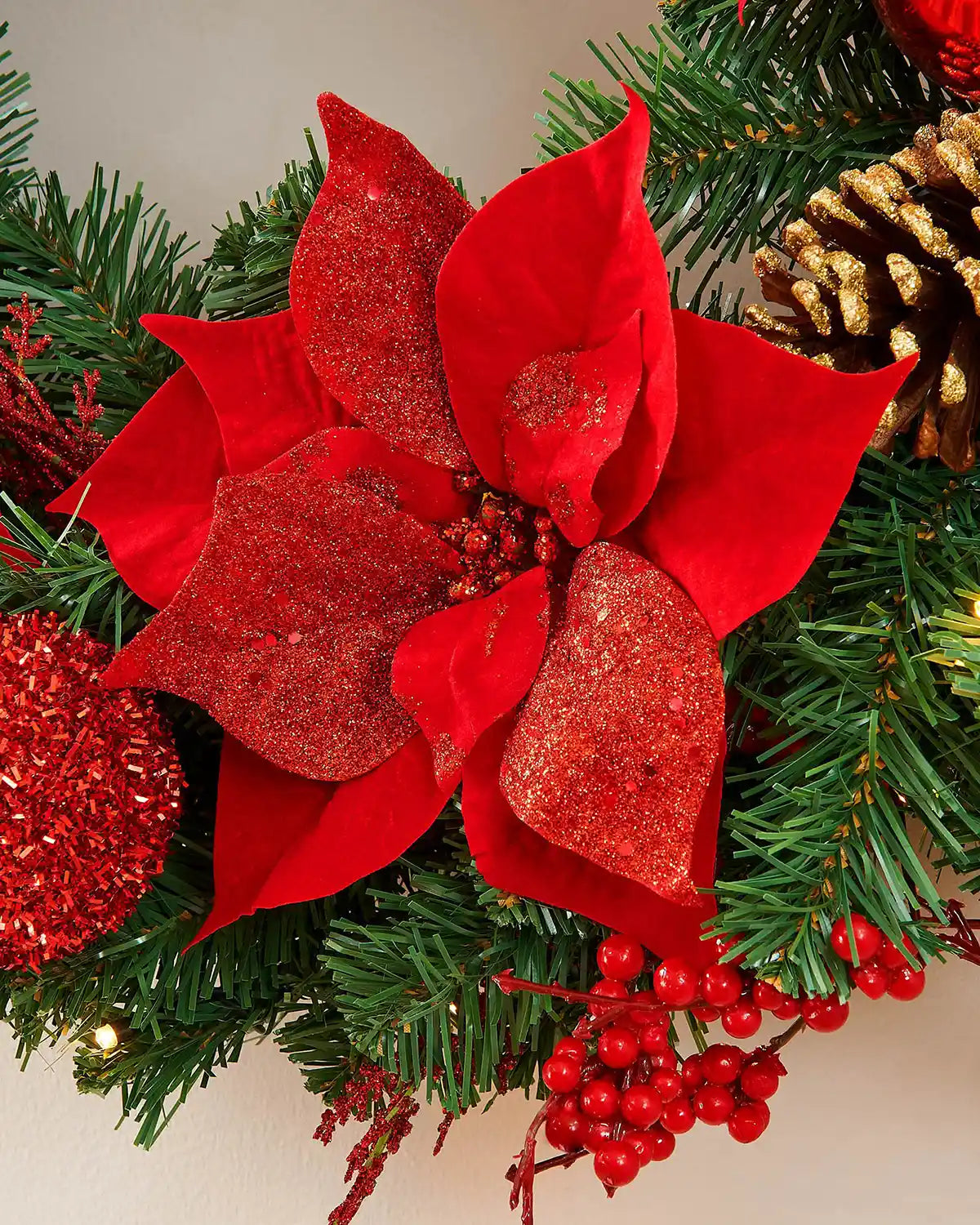 Close-up of a red poinsettia, berries and gold-tipped pinecone on the pre-lit Christmas wreath