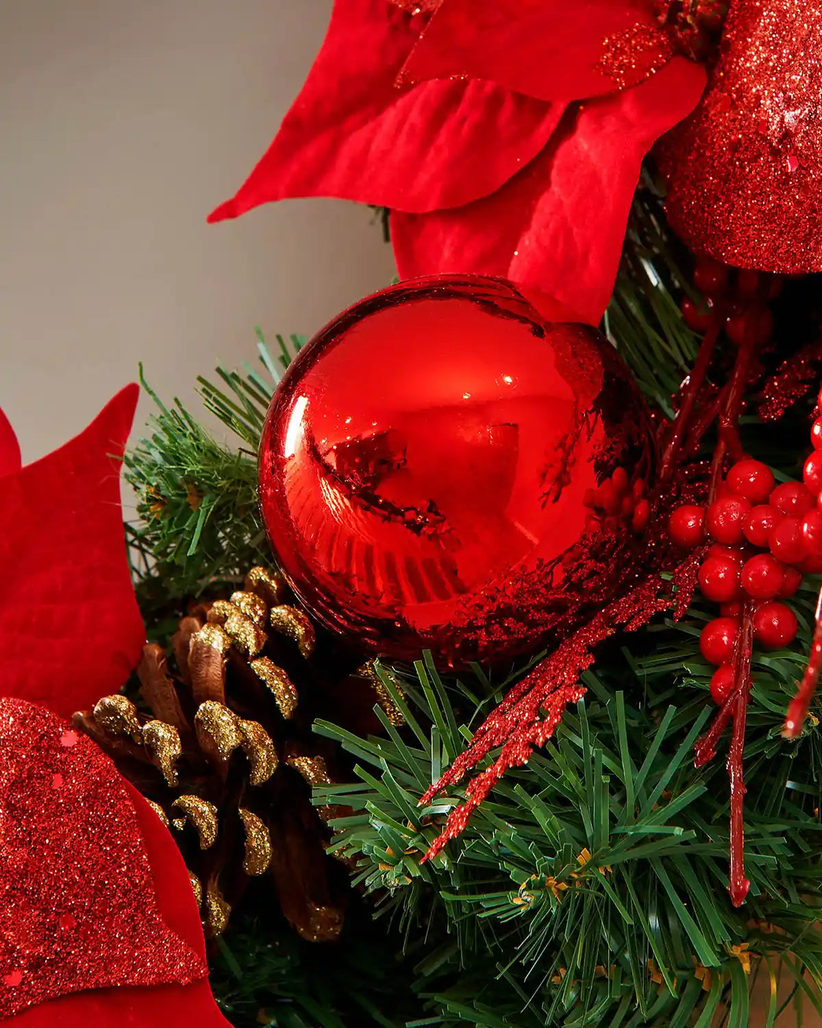 Close-up of a red bauble, berries and gold-tipped pinecone on the pre-lit Christmas wreath