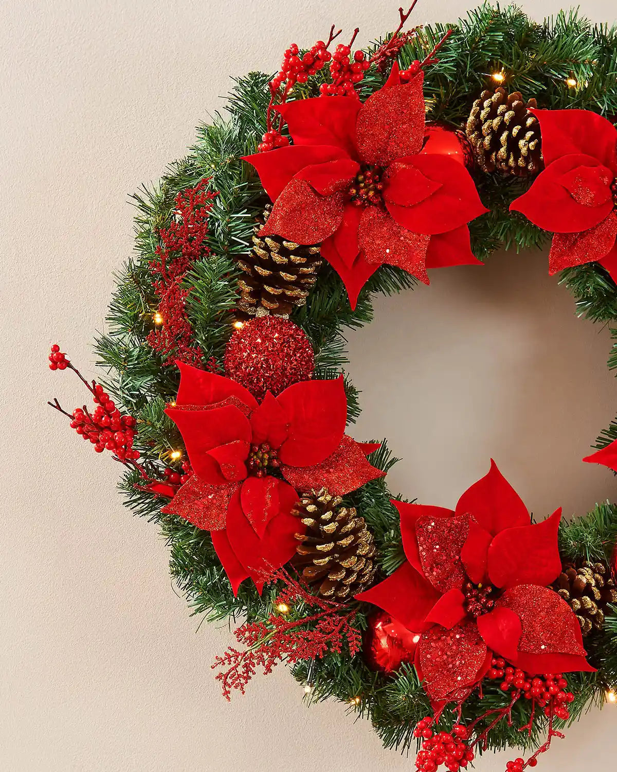 Extra thick red and gold pre-lit Christmas wreath styled on a wall with warm white lights