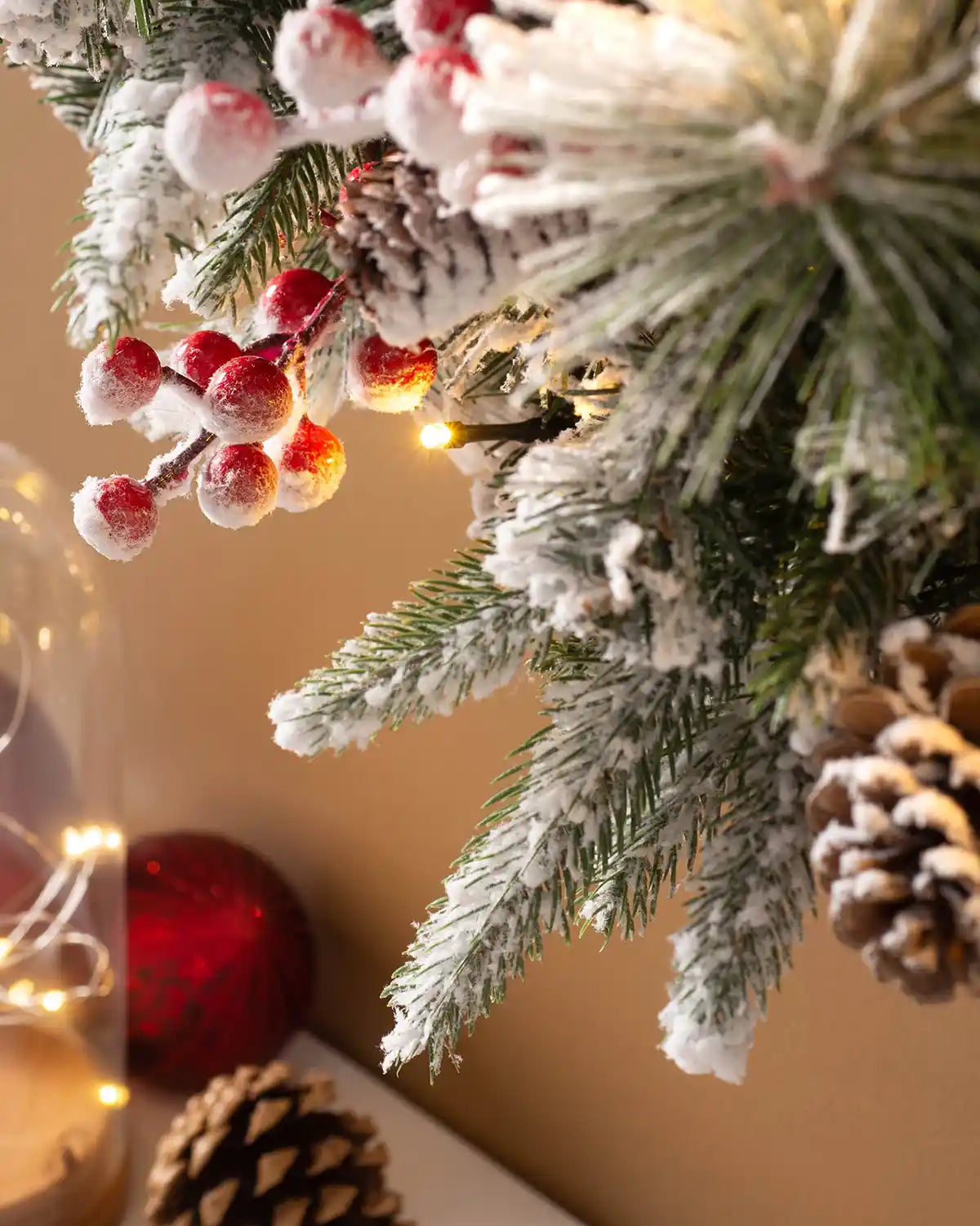 Close-up of frosted red berries, pinecones and warm white lights on the snow-flocked Christmas wreath