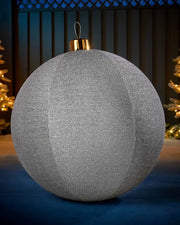 Large silver 76cm inflatable tinsel Christmas bauble with a gold cap in an outdoor festive display.
