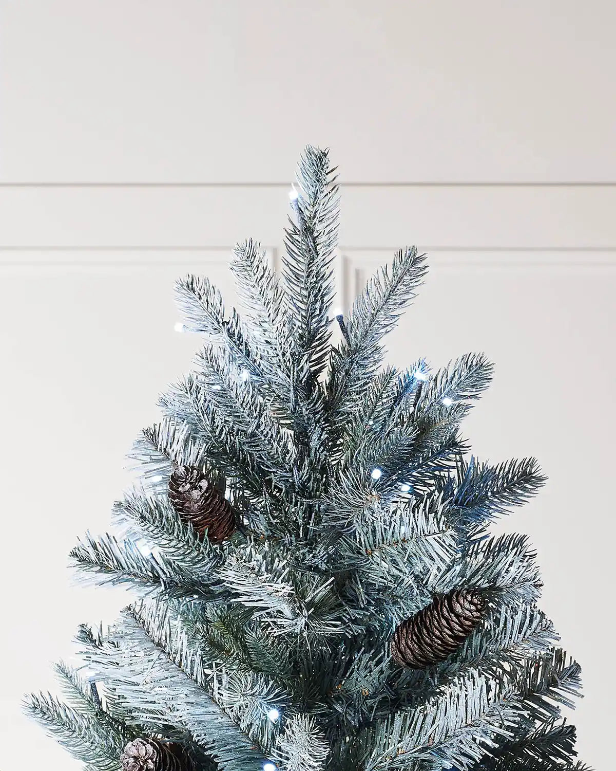 Top section of a 7 ft frosted Edwardian Spruce Christmas tree with pinecones and bright white lights