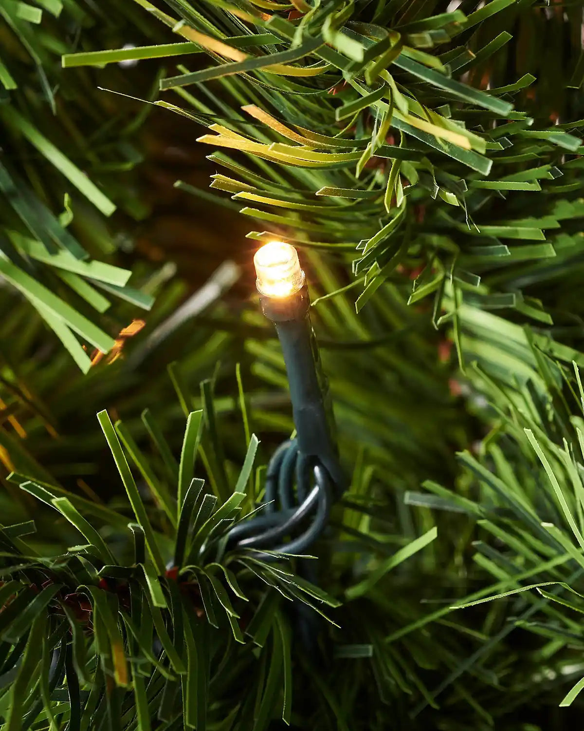 Close-up of a warm white LED light woven through green PVC branches on an emerald spruce tree