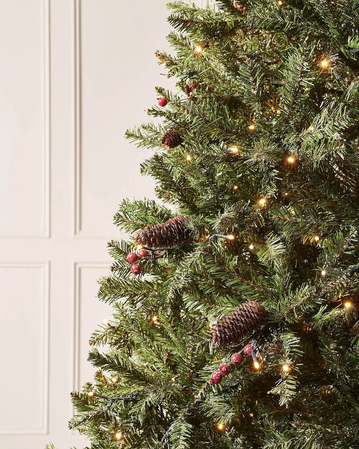 Close-up of frosted Christmas tree branches with pinecones, red berries and warm white lights