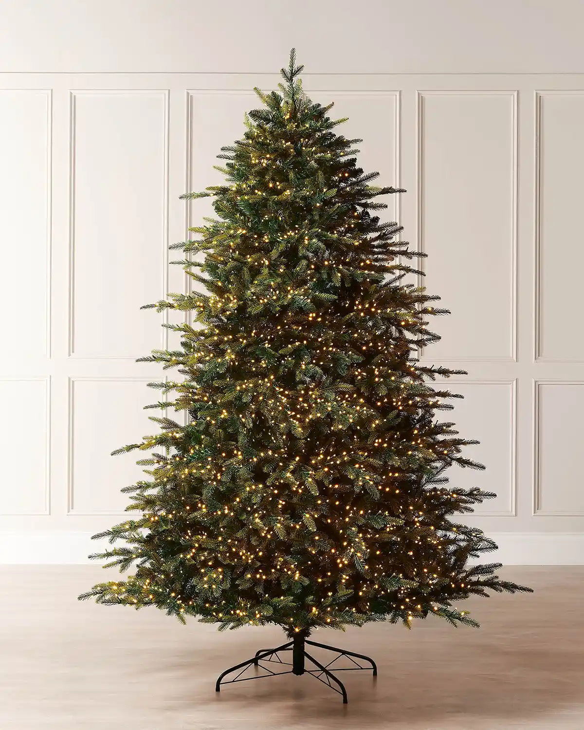 7ft pre-lit Highland fir Christmas tree displayed indoors with warm white LEDs, full green branches and a metal tree stand.