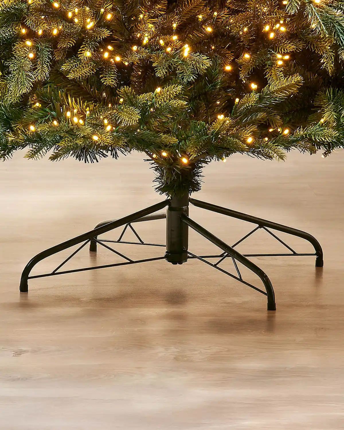 Close-up of the metal tree stand beneath the 7ft pre-lit Highland fir Christmas tree on an indoor wooden floor.