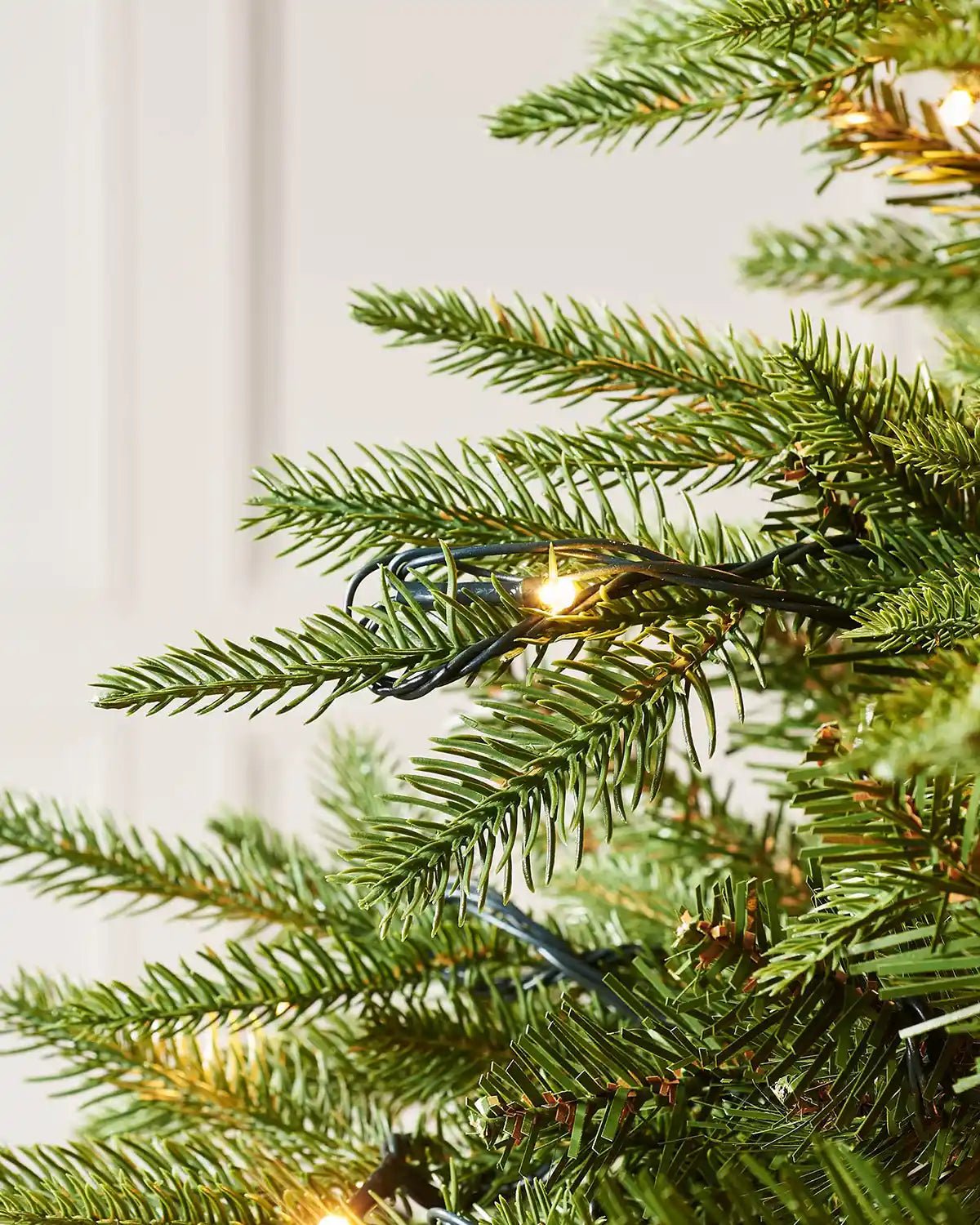 Close-up of a warm white LED light and black cable resting on green Royal Fir branches