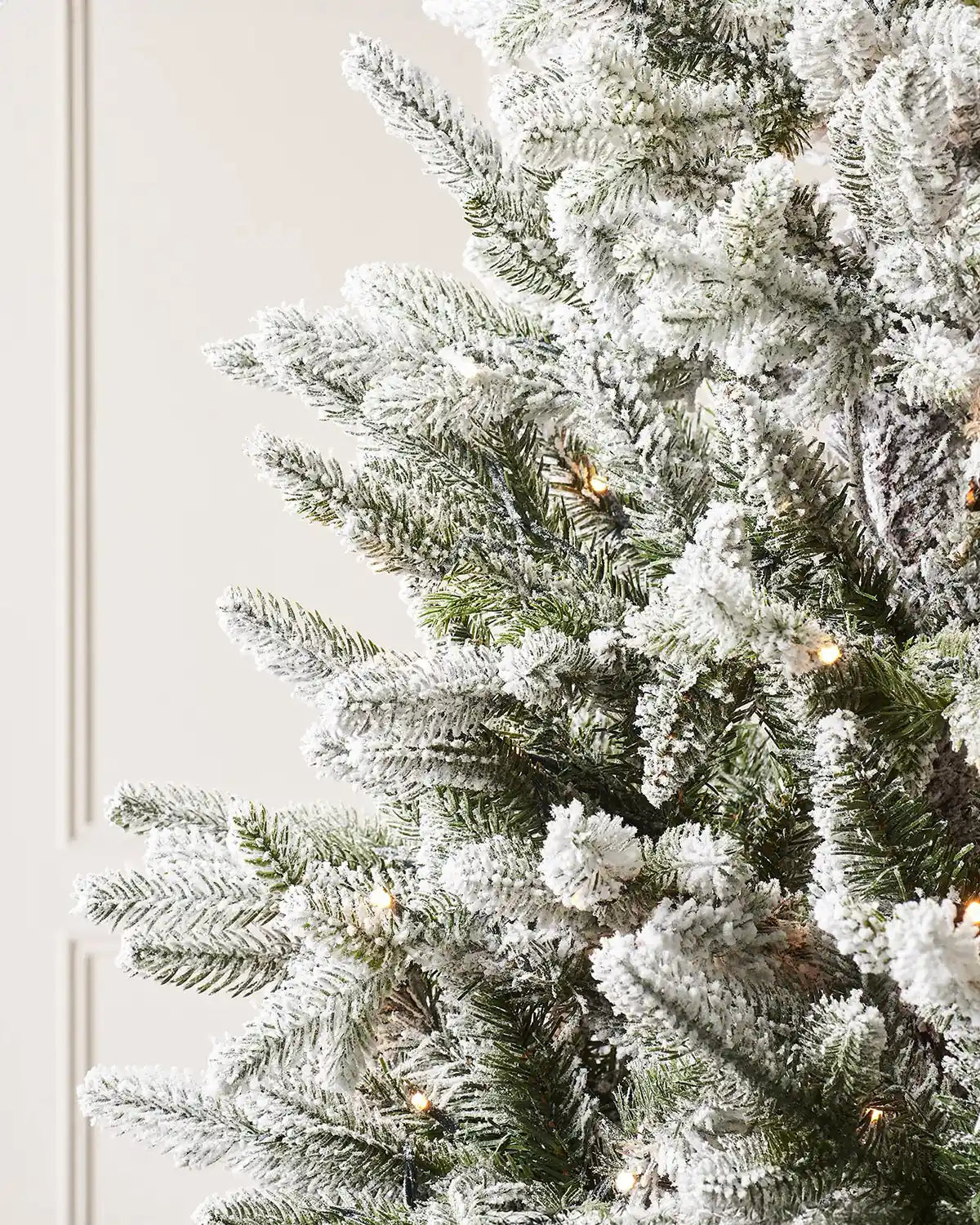 Close-up of snow flocked Christmas tree branches with warm white LED lights and dense frosted foliage