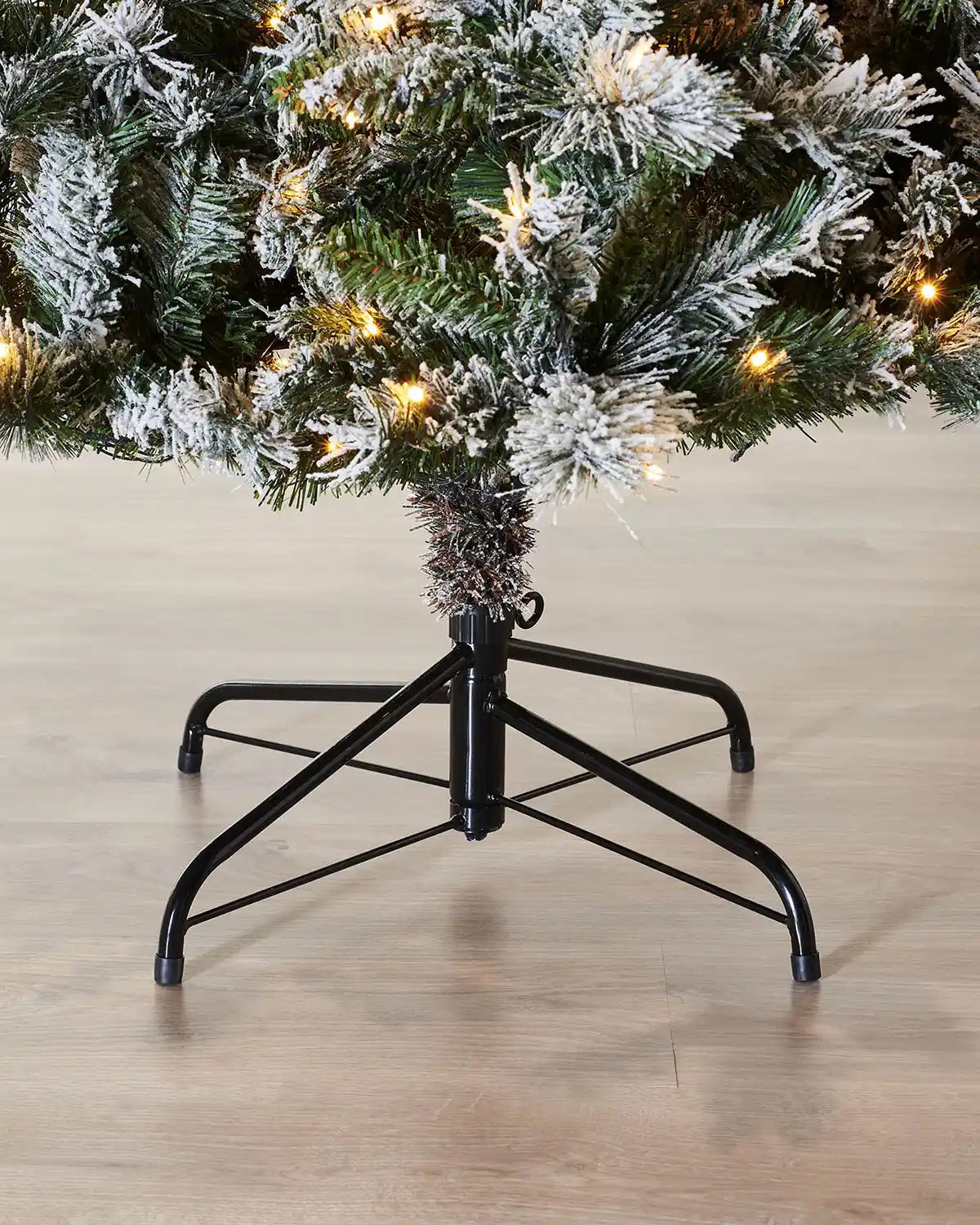 Close-up of the metal tree stand beneath a 7 ft pre-lit slim snow-flocked spruce Christmas tree