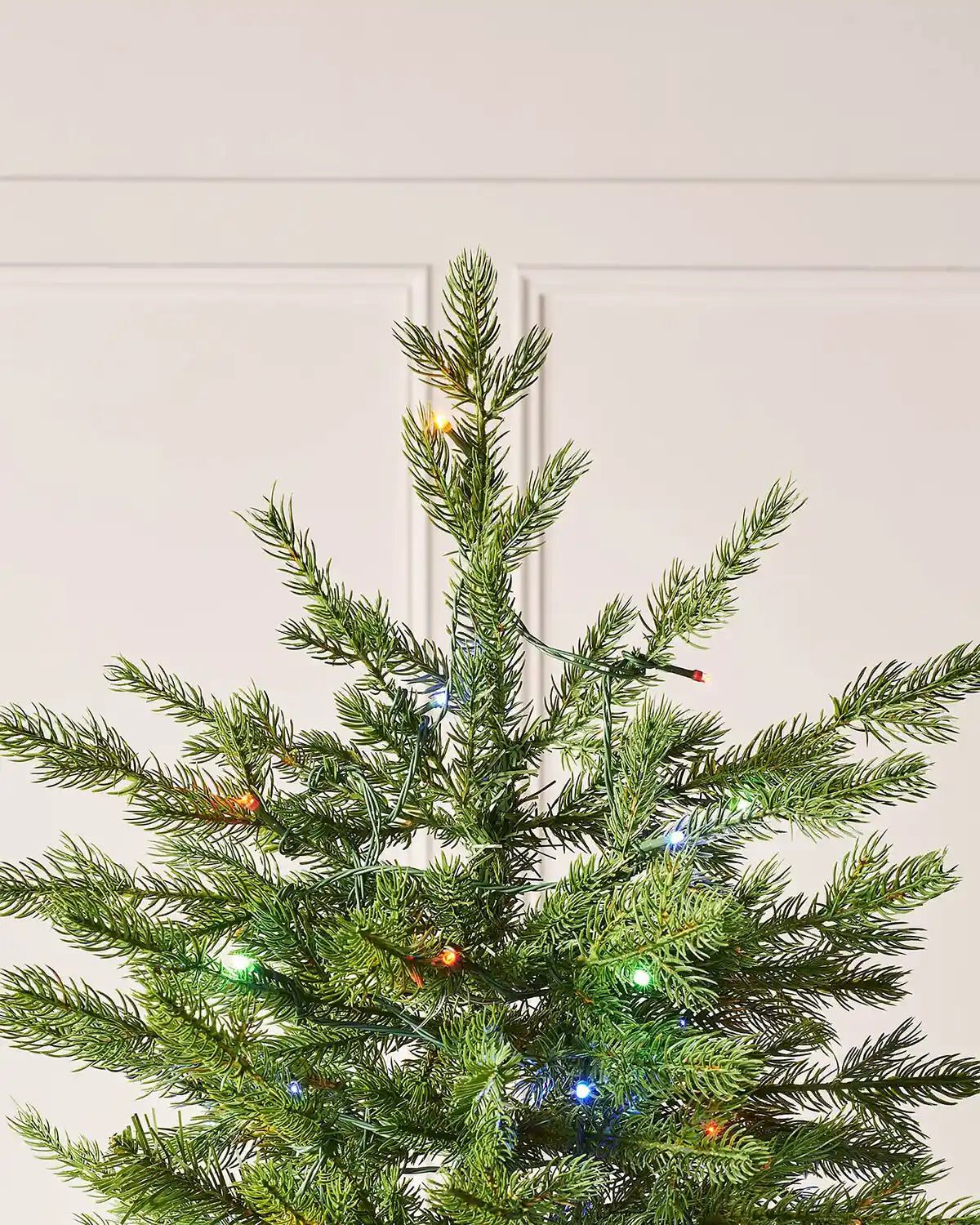 Top section of 7ft Windsor Fir Christmas tree with natural green branch tips, dual multicolour LEDs and slim realistic artificial fir shape against a panelled wall
