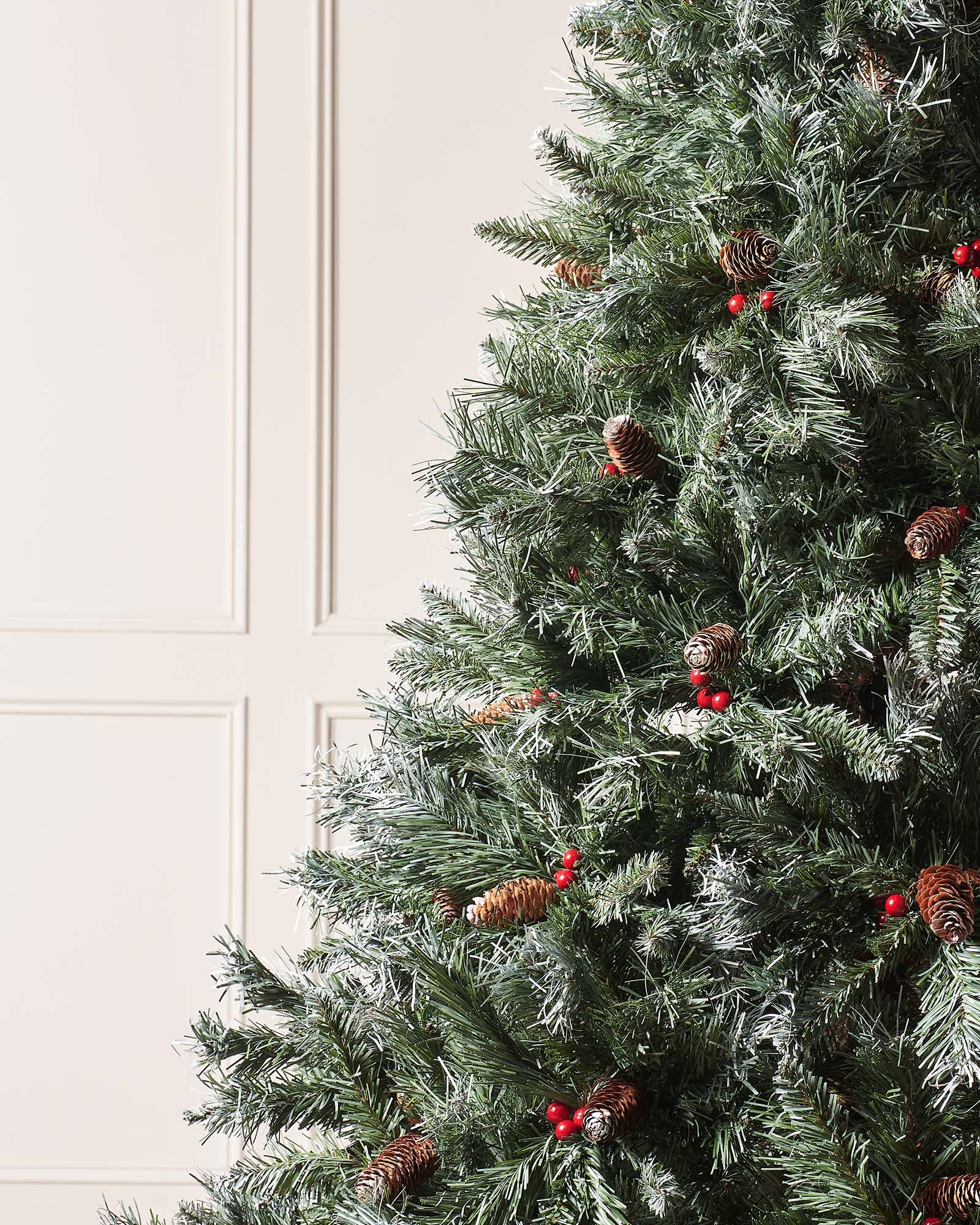 Close-up of a 7 ft Scandinavian blue spruce Christmas tree with frosted branches, pinecones and red berries