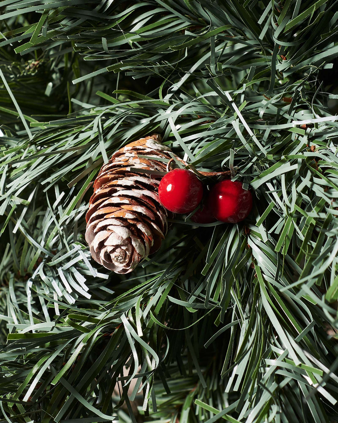 Close-up of a frosted pinecone and red berries on a Scandinavian blue spruce Christmas tree