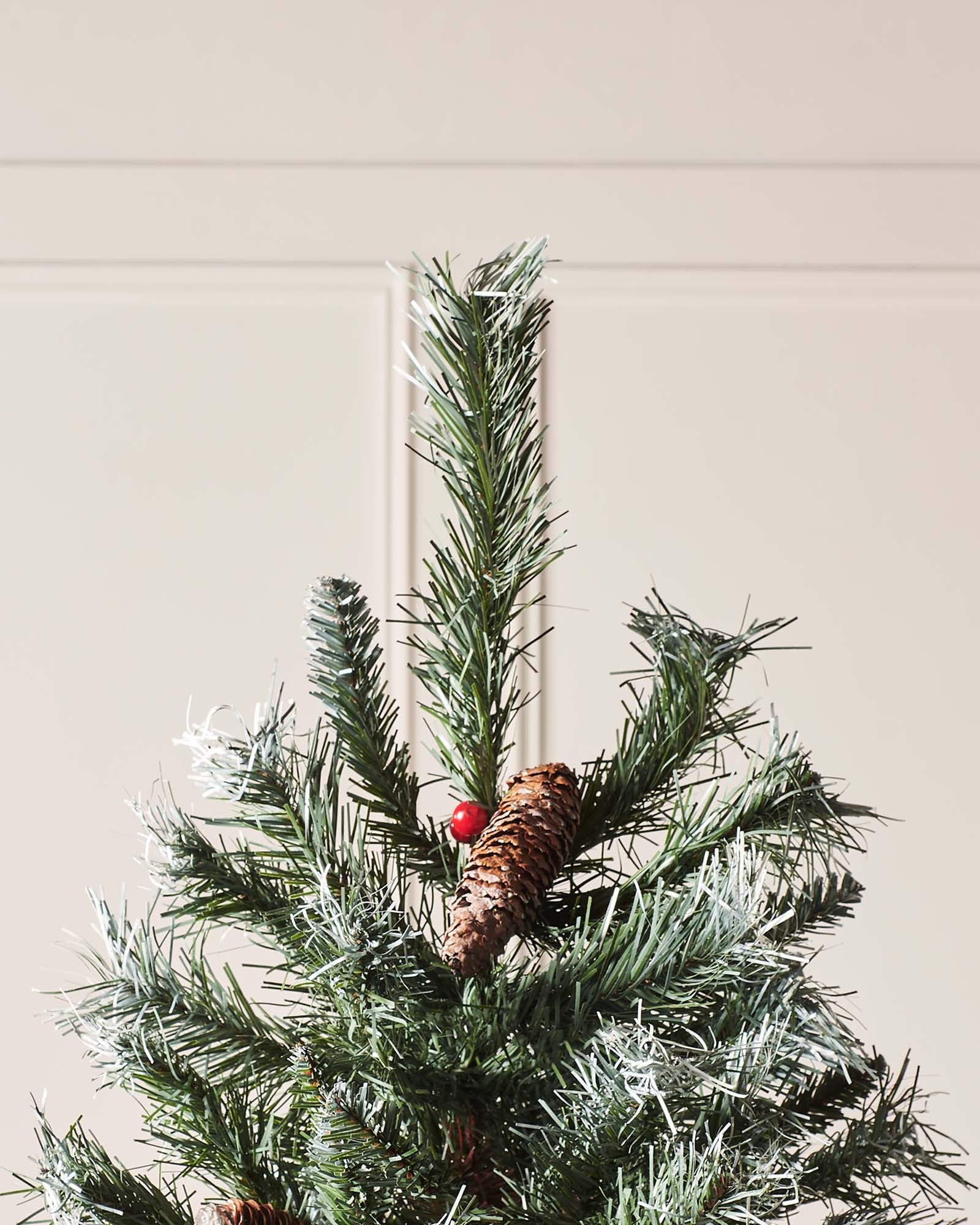 Top section of a Scandinavian blue spruce Christmas tree with frosted tips, pinecone and red berry detail
