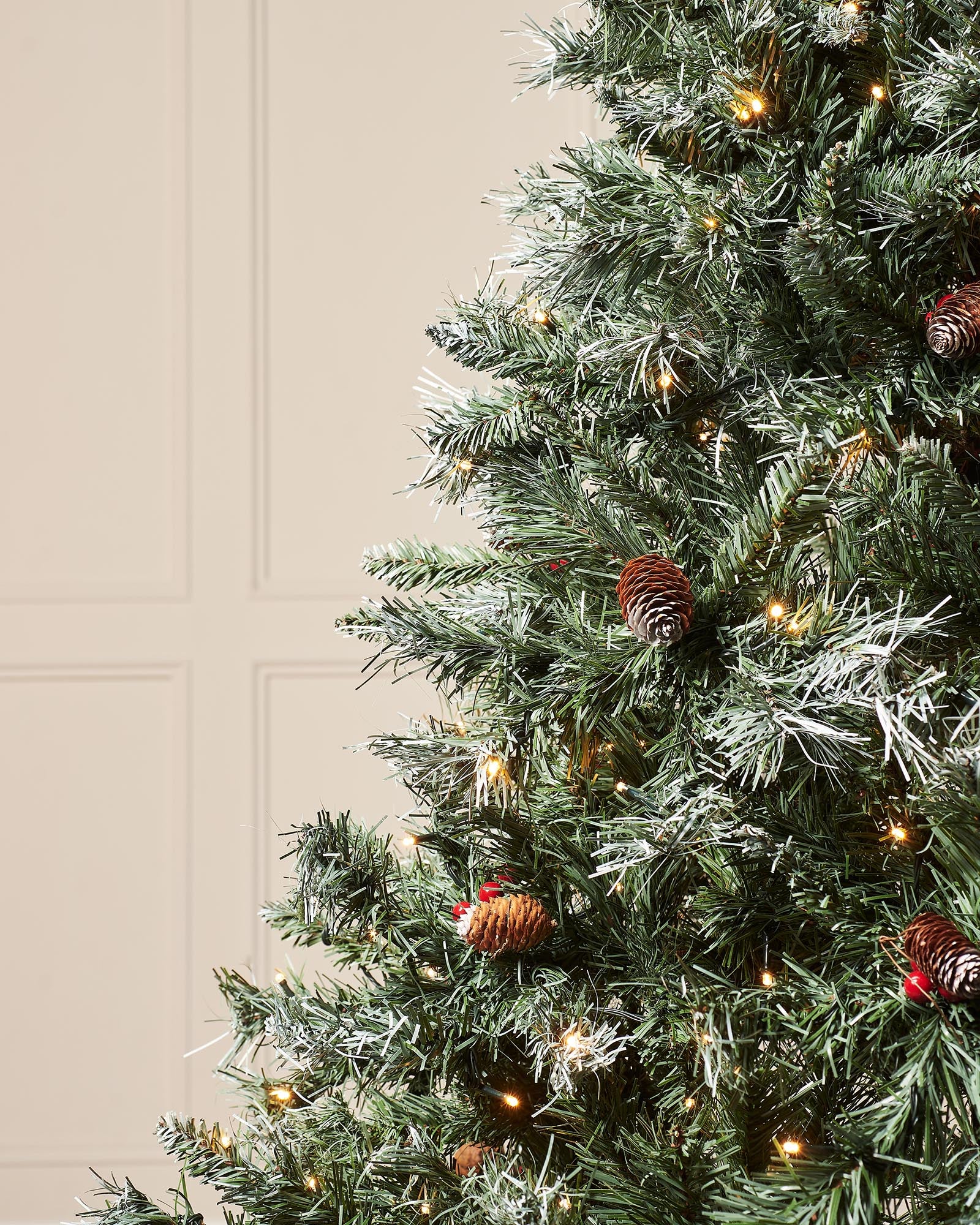 Close-up of frosted green branches with pinecones, red berries and warm white LEDs