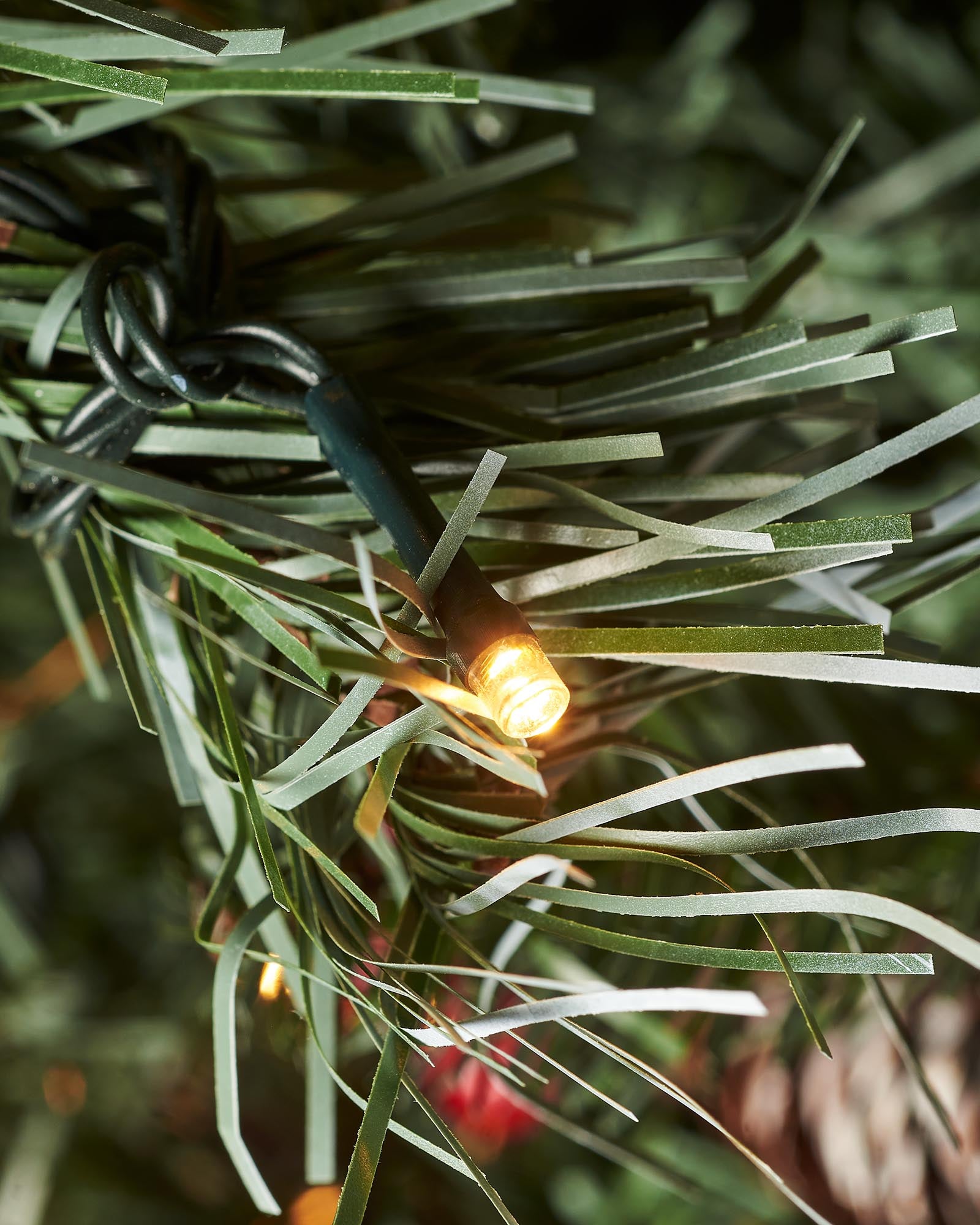 Warm white LED light nestled among frosted green artificial Christmas tree branches