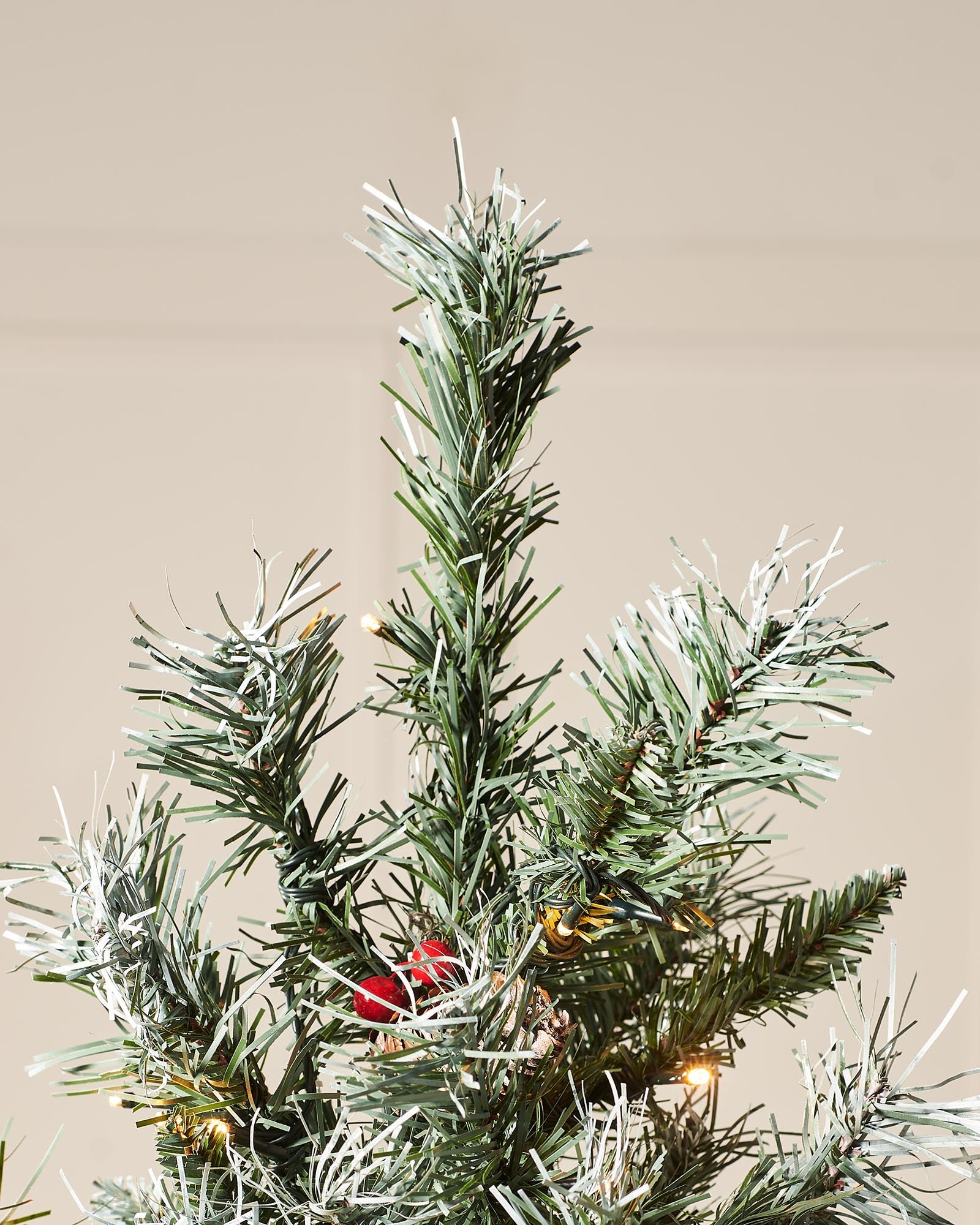 Top section of a frosted Scandinavian spruce Christmas tree with warm white lights and red berries