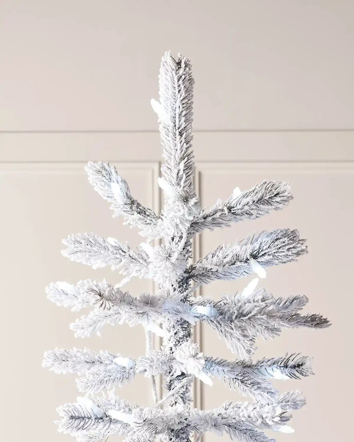 Top branch detail of 7ft snow flocked spruce Christmas tree with snowy foliage and cool white LEDs