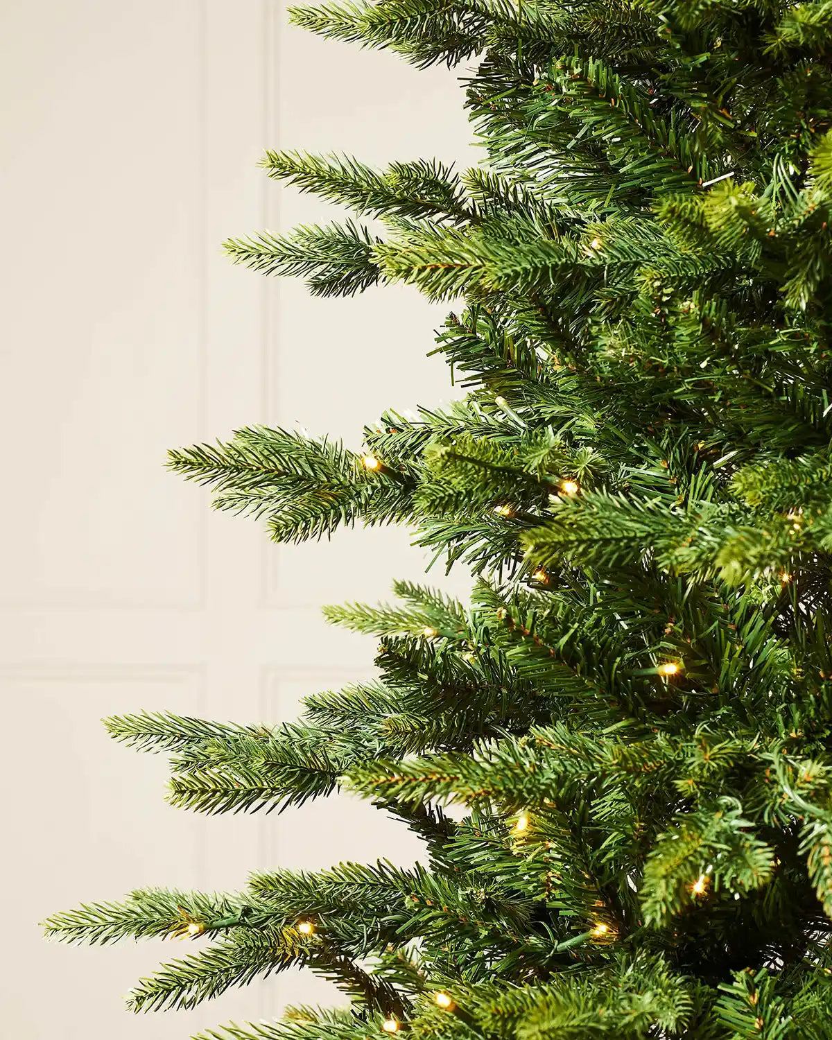 Close up of the PE and PVC and lights on a 7ft Himalayan Fir Christmas tree with lights with cream panel textured wallpaper.
