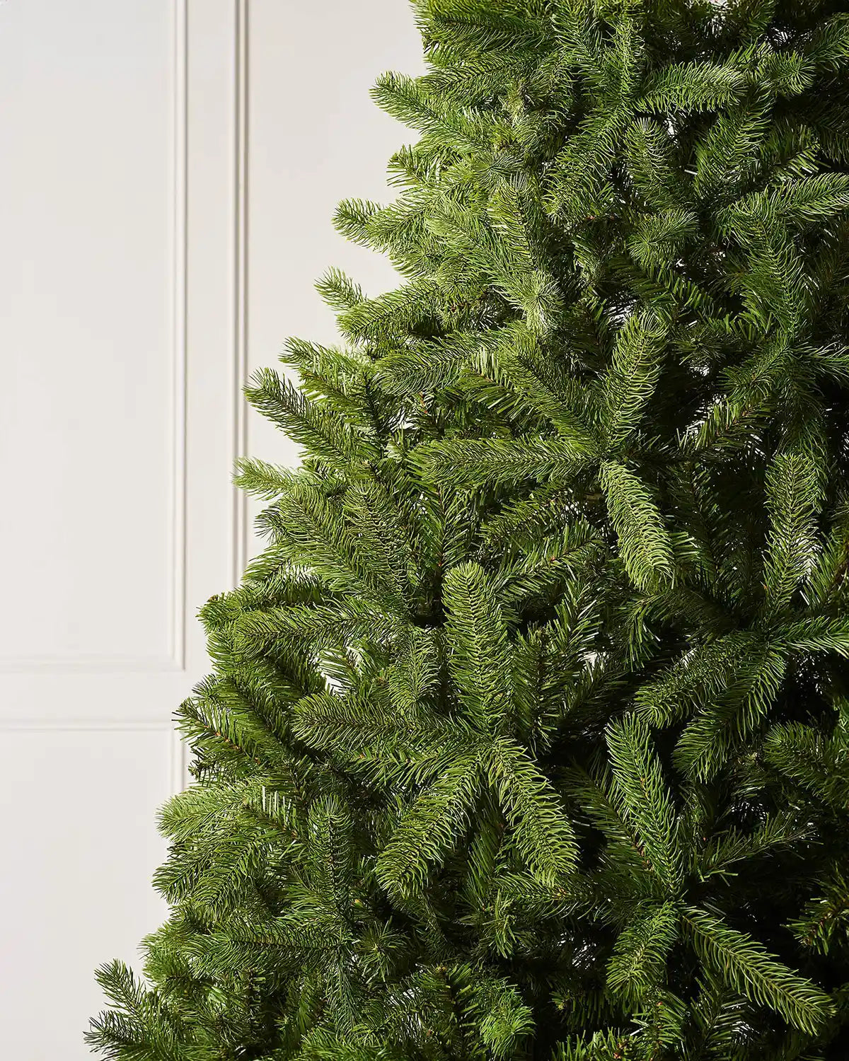 Close up of the PE and PVC tips on a 7ft Mixed Pine Christmas tree  with cream panel textured wallpaper.