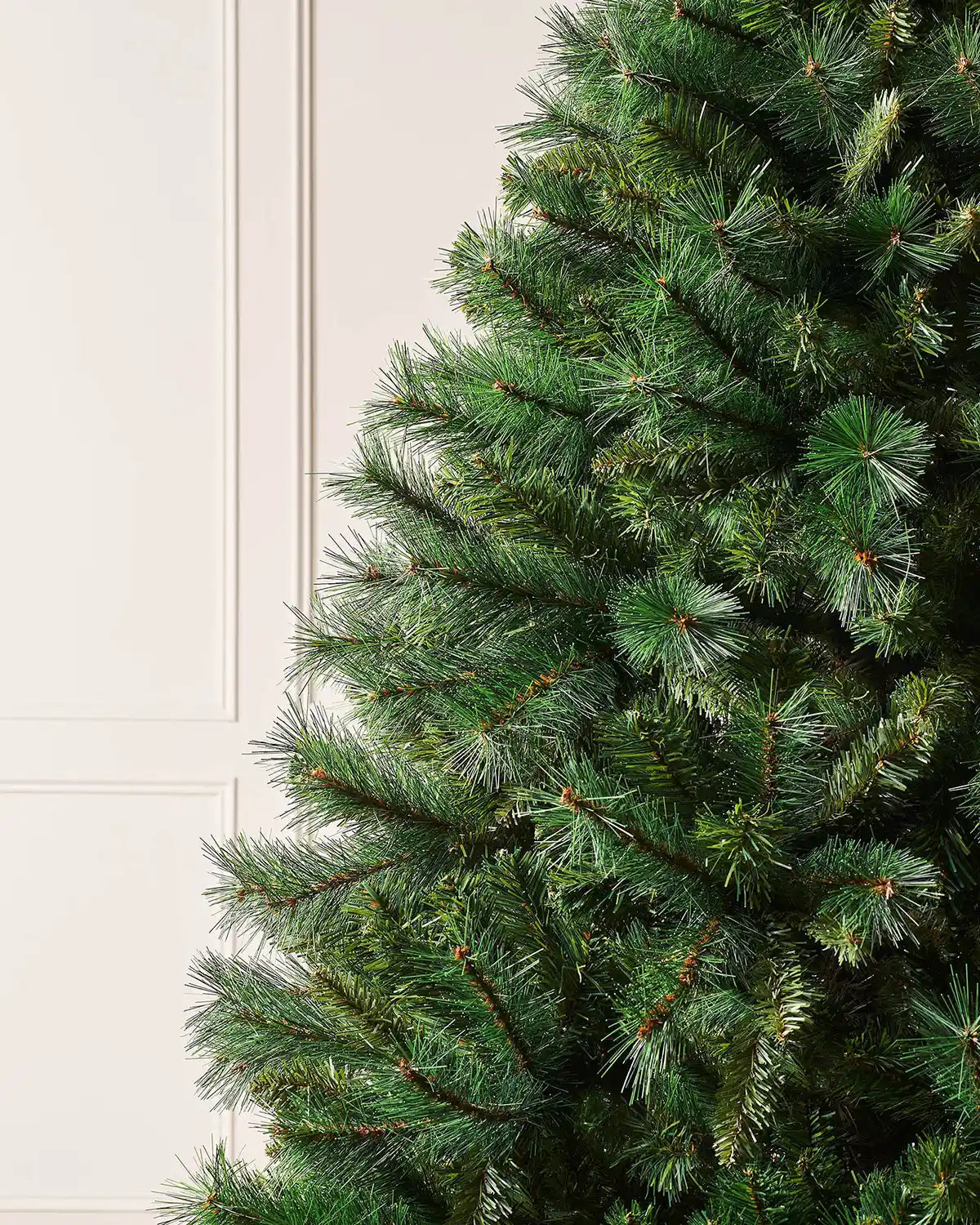 Close up of the PE and PVC tips on a 7ft Victorian Pine Christmas tree  with cream panel textured wallpaper.
