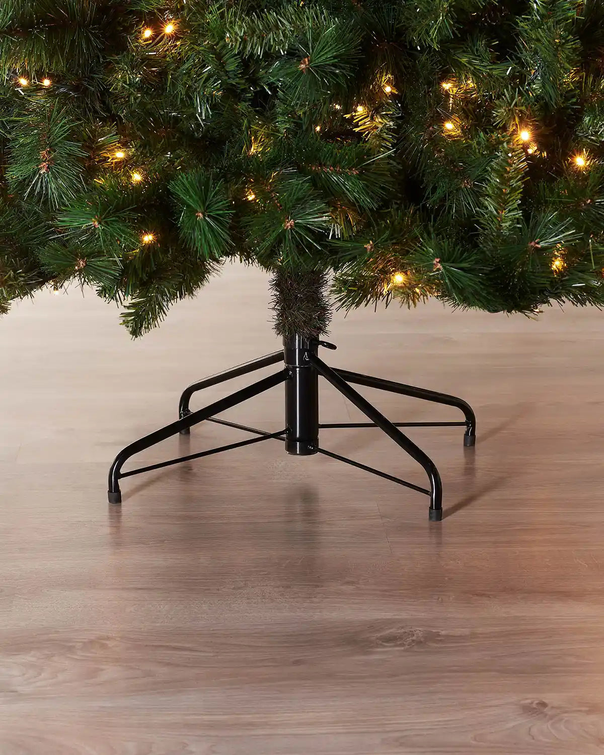 Close up of the base of 7ft Victorian Pine Christmas tree with lights and Black Tree Stand 
