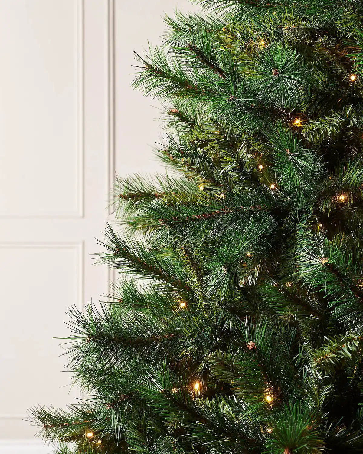 Close up of the PE and PVC and lights on a 7ft Victorian Pine Christmas tree with lights  with cream panel textured wallpaper.