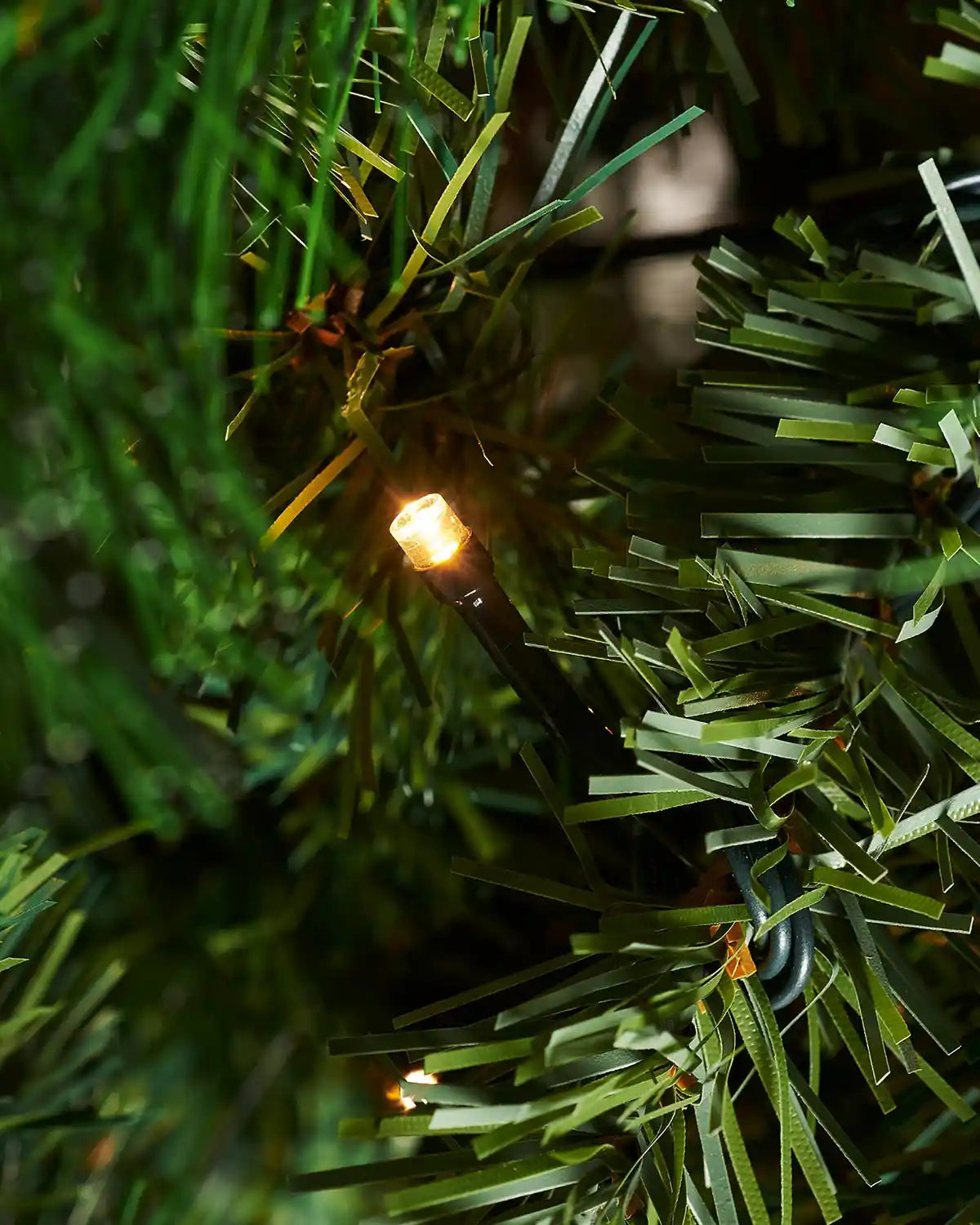 Close up of a single lit bulb on a 7ft Victorian Pine Christmas Tree with PE and PVC tips.
