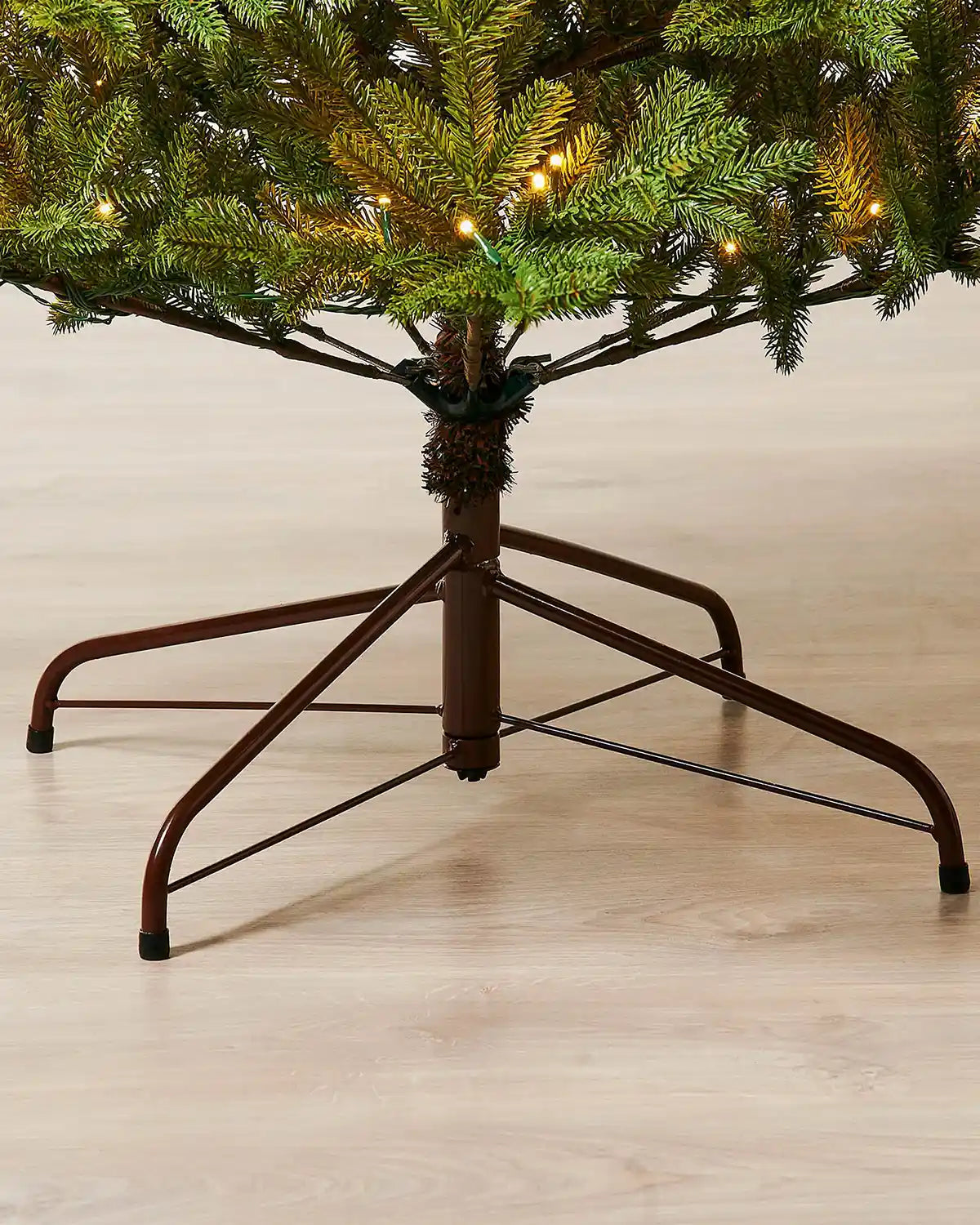 Close-up of 7ft pre-lit nordic pine Christmas tree brown stand on light wood flooring