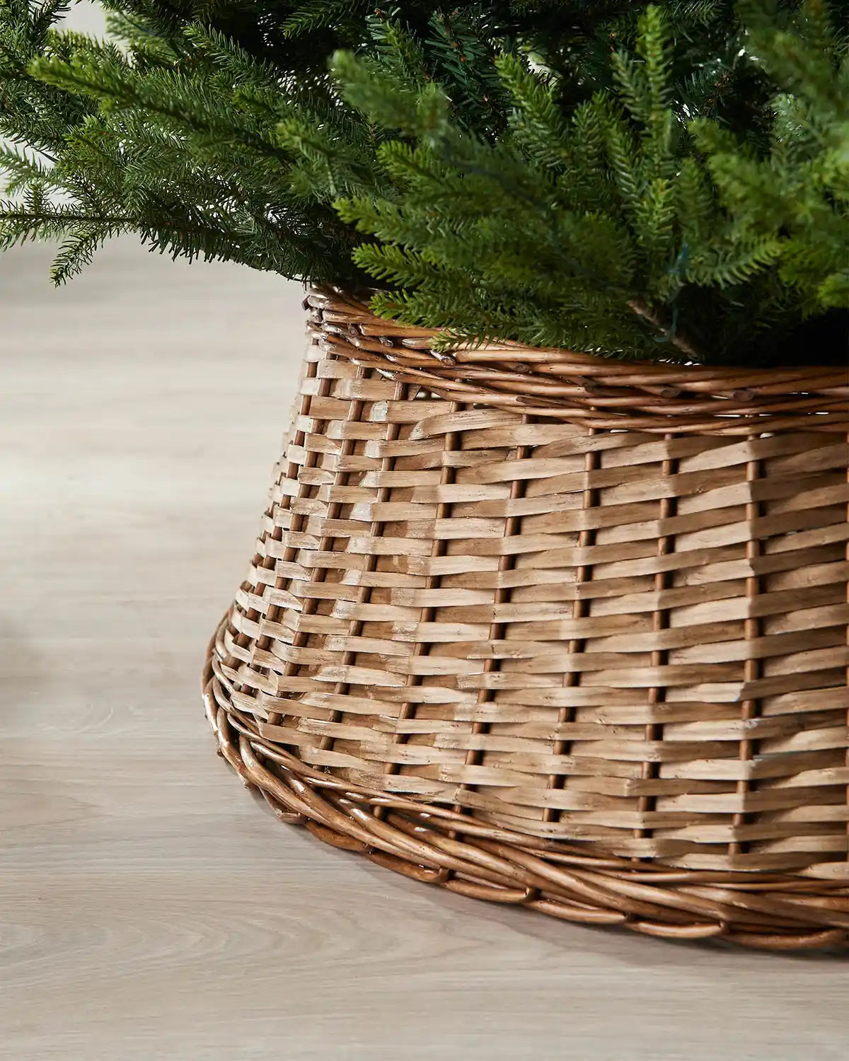 Close-up of the 85cm brown wicker tree collar showing the woven rattan texture beneath green Christmas tree branches.