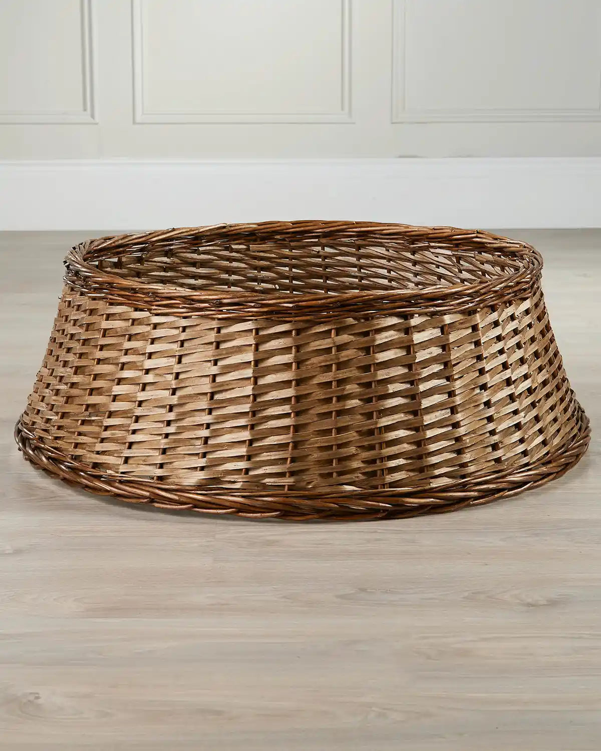 85cm brown wicker tree collar displayed indoors on a wooden floor, showing its tapered shape and open top.