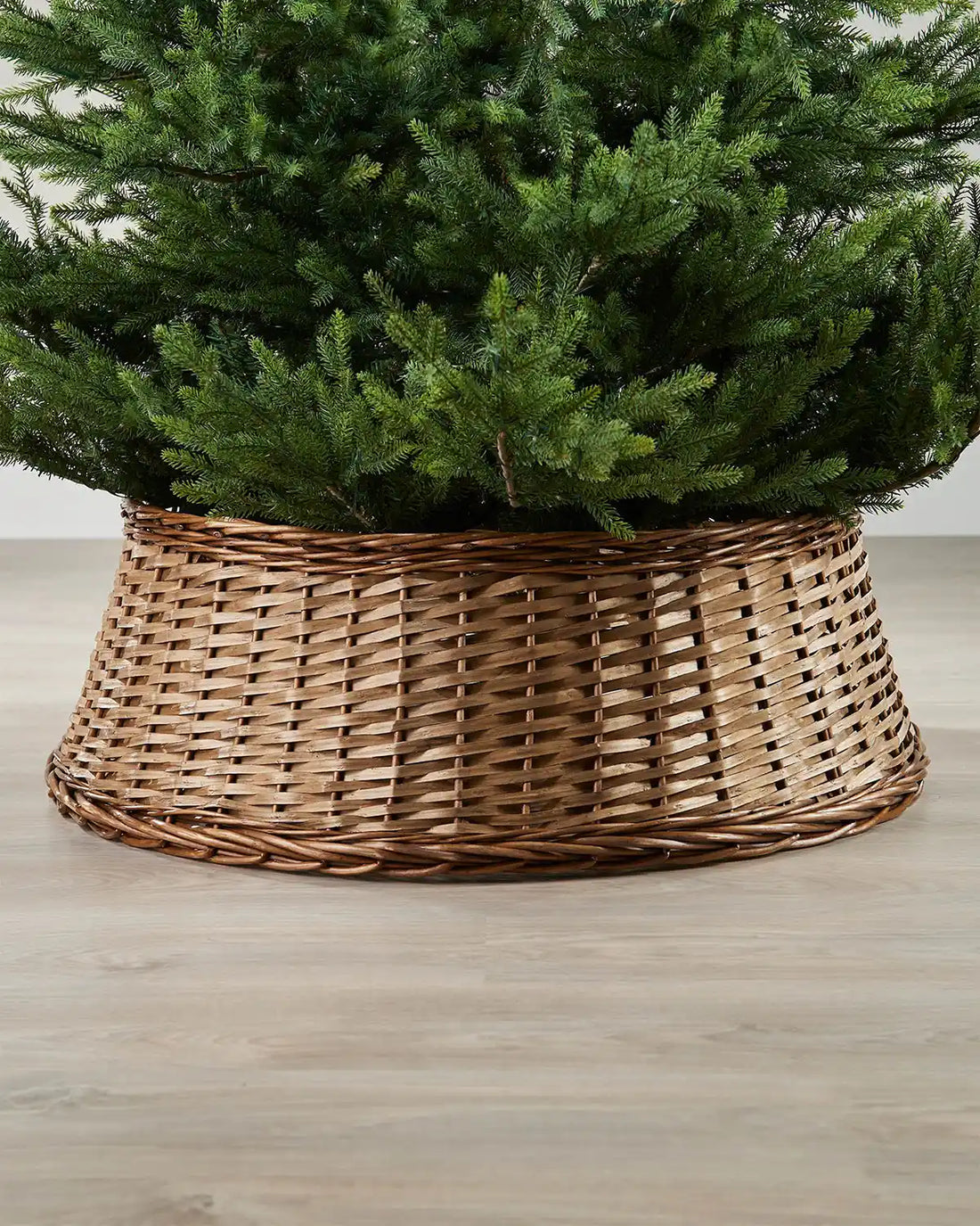85cm brown wicker tree collar placed around the base of a Christmas tree on an indoor wooden floor.