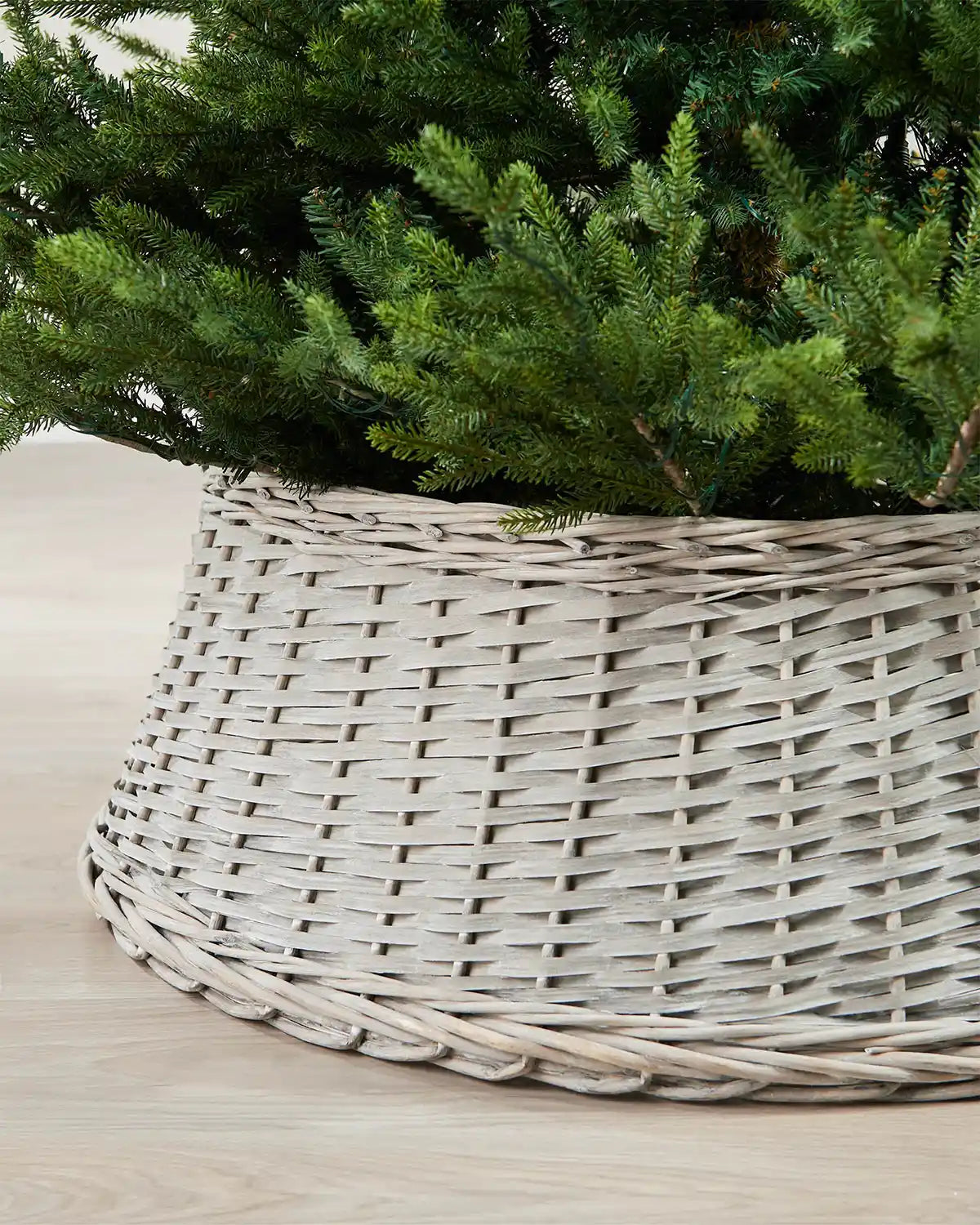 Close-up of the 85cm grey wicker tree collar showing the woven rattan texture beneath green Christmas tree branches.