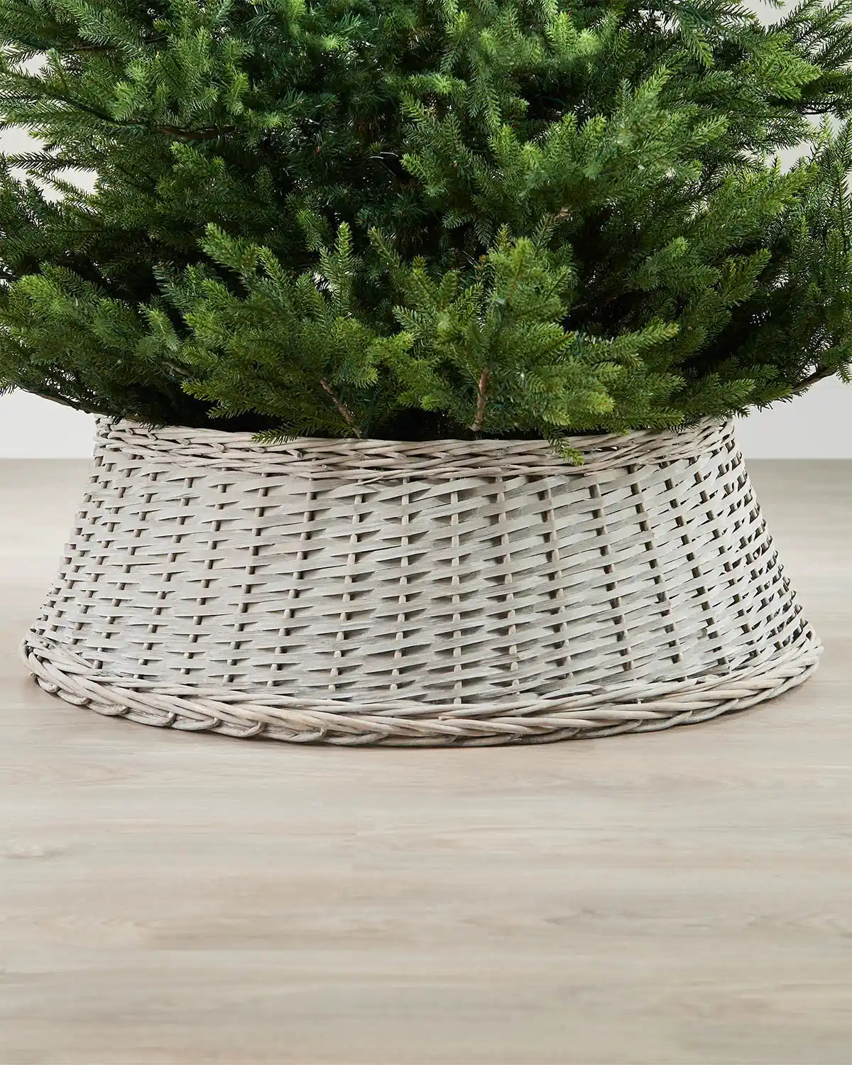 85cm grey wicker tree collar placed around the base of a Christmas tree on an indoor wooden floor.