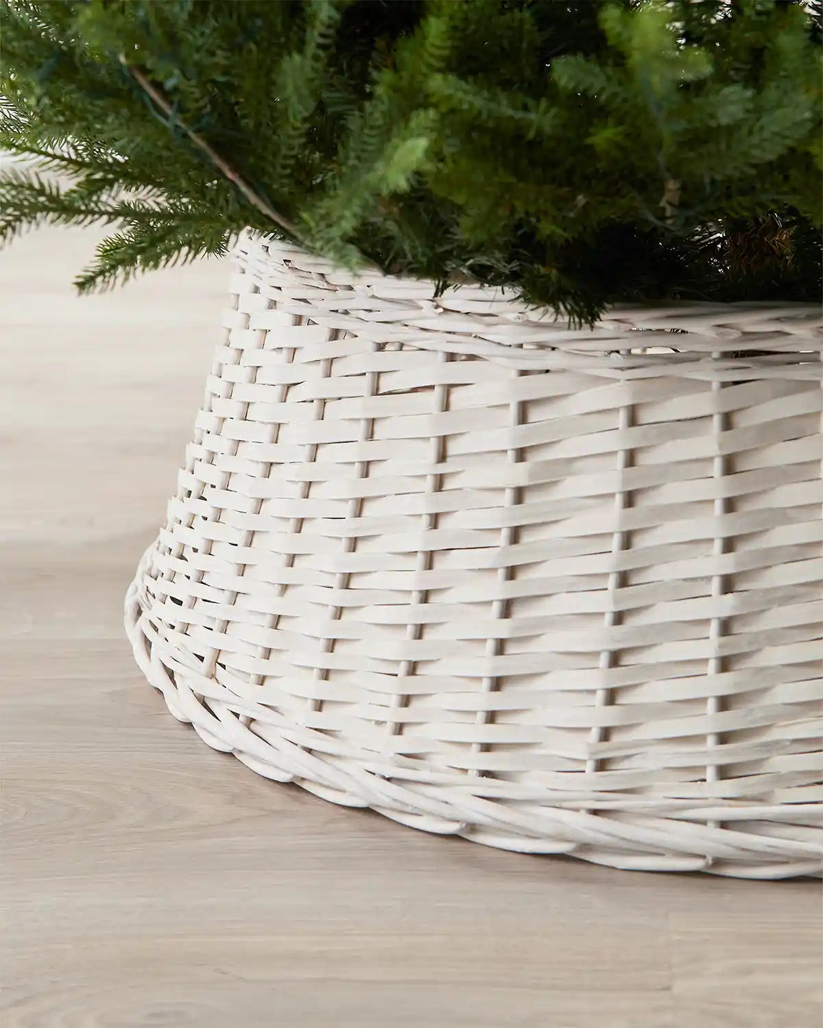 Close-up of the 85cm off-white wicker tree collar showing the woven rattan texture beneath green Christmas tree branches.
