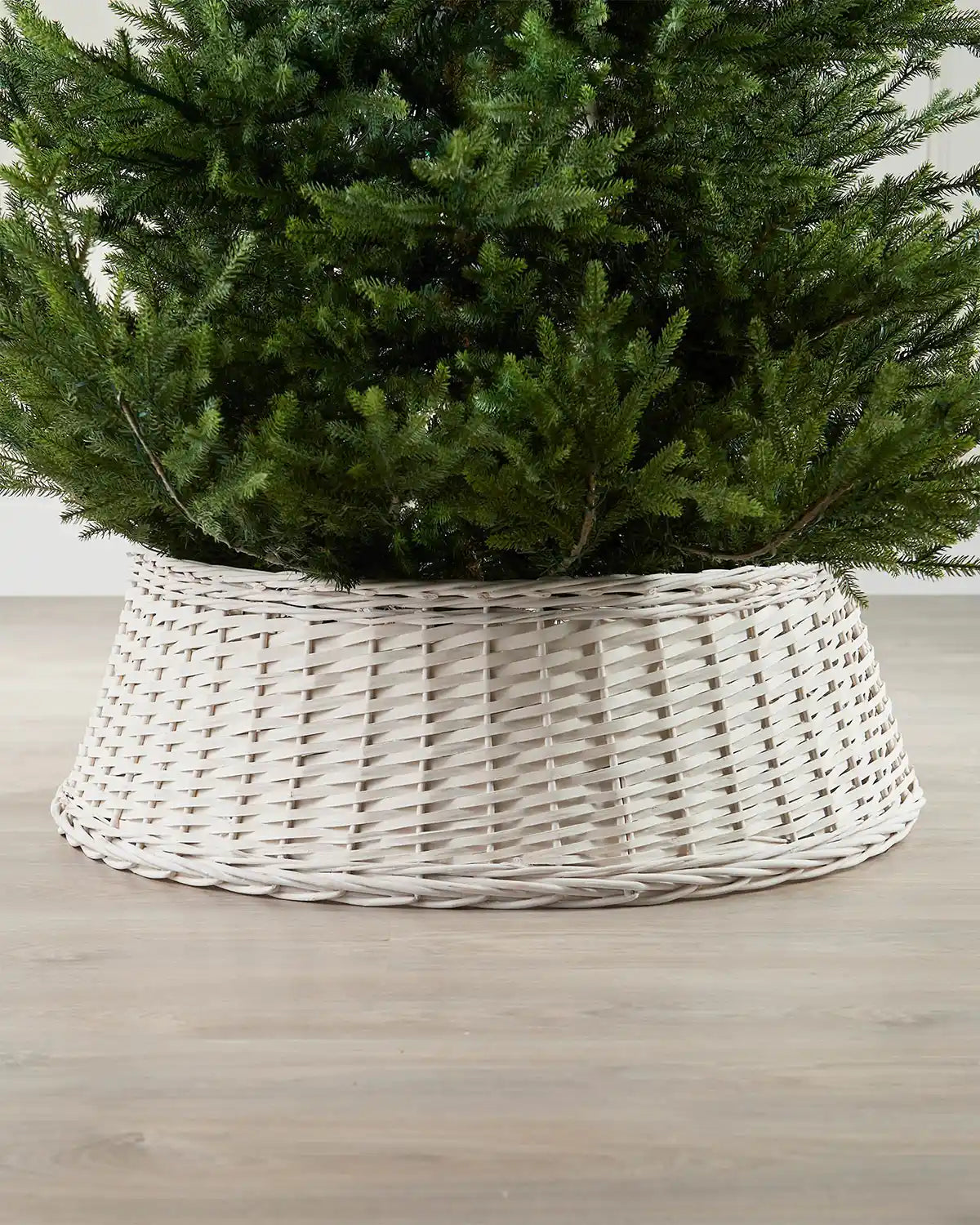 85cm off-white wicker tree collar placed around the base of a Christmas tree on an indoor wooden floor.