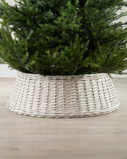 85cm off-white wicker tree collar placed around the base of a Christmas tree on an indoor wooden floor.